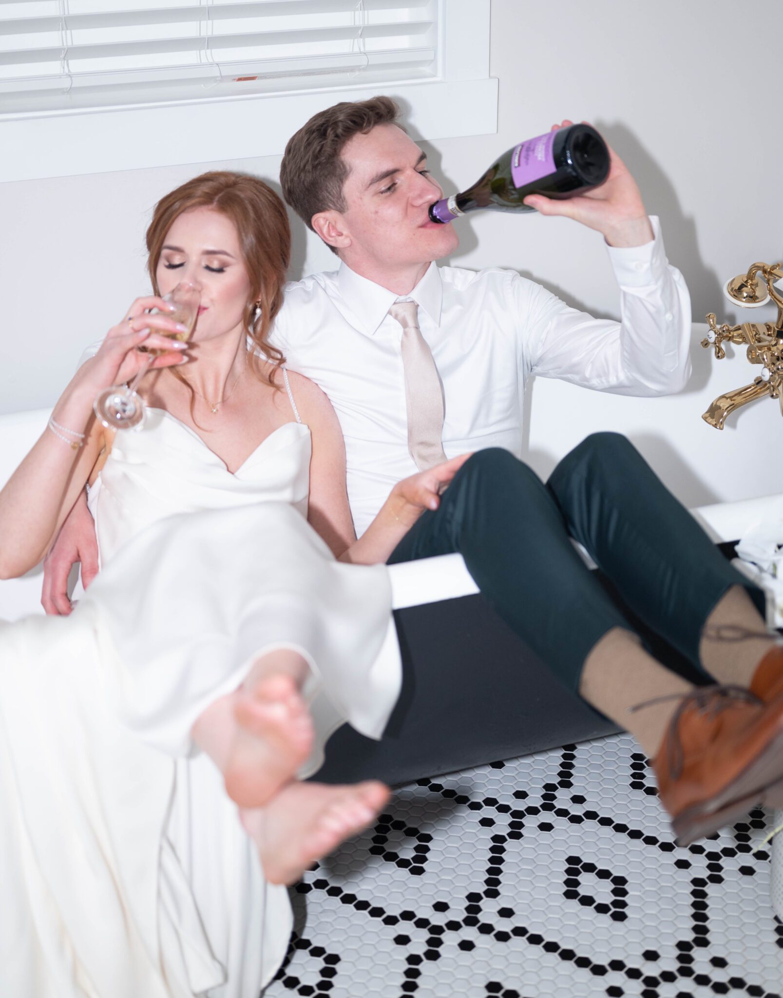 Bride and groom enjoy a sip of their champagne while relaxing in the getting ready suite clawfoot bathtub. Classic Calgary Wedding with Bright Colours & Bathtub Portraits