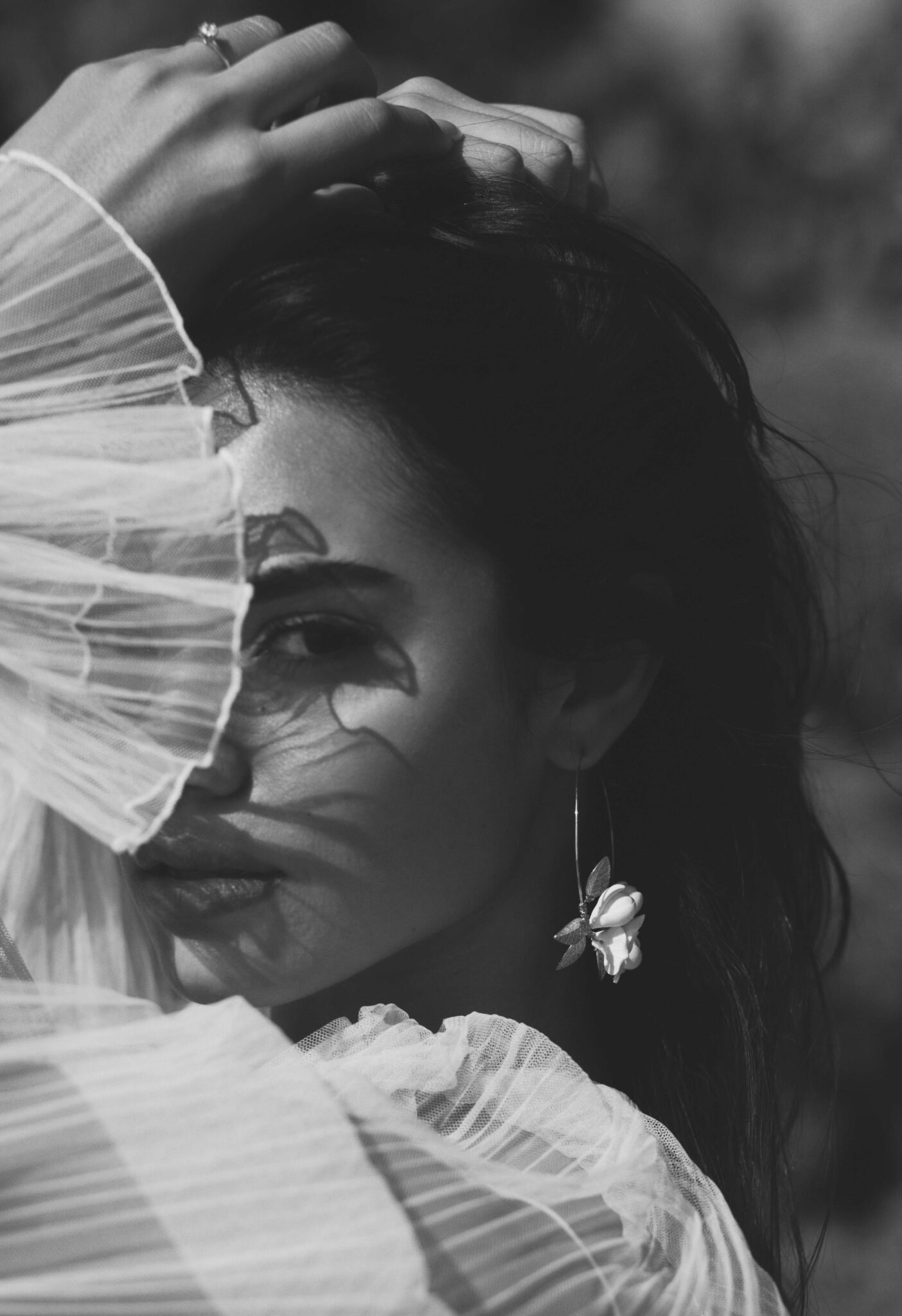 Black and white portrait of bride in Mexico, while covering her face with the elegant tulle sleeves, bride is wearing floral detailed earrings. 