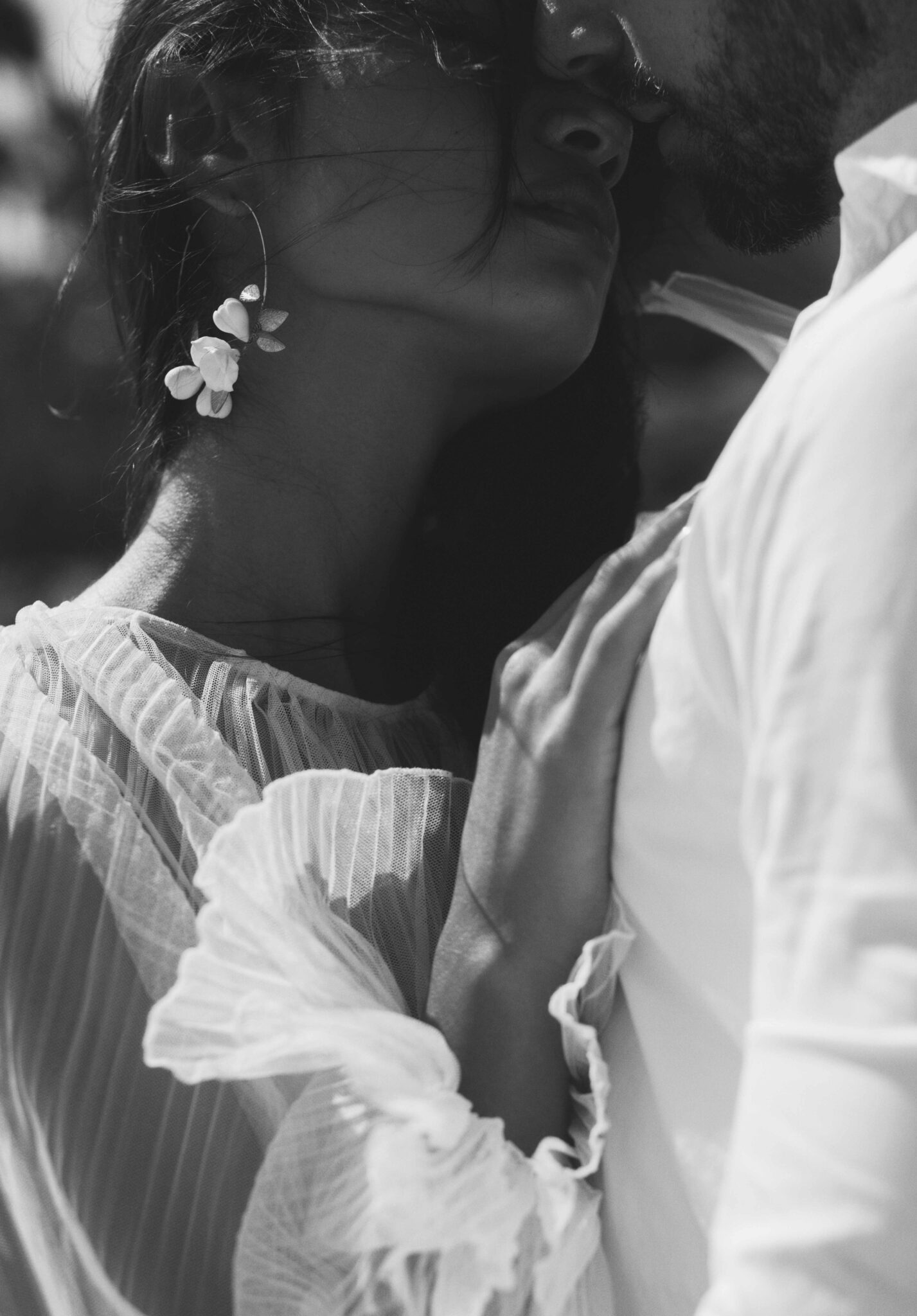 Intimate portrait of bride and groom, with bride's hair blowing in the wind, featuring a floral-detailed bridal earring, and elegant tulle sleeves. 