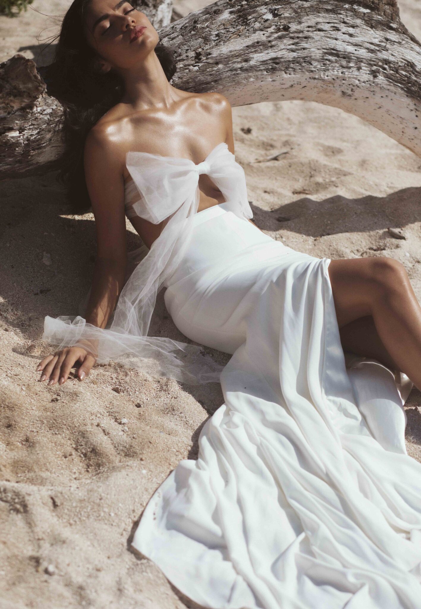Sun-kissed bridal portrait, featuring a chic tulle bow-tied top and skirt set, laying on the sandy shores in Mexico, Storm-inspired bridal inspiration from Tempête with an effortless & free-spirited nature. 