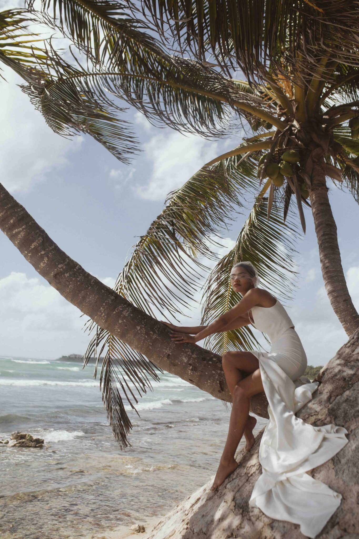 Bride in chic gown leaning against a palm tree in Mexico, Storm-inspired bridal inspiration from Tempête with an effortless & free-spirited nature. 