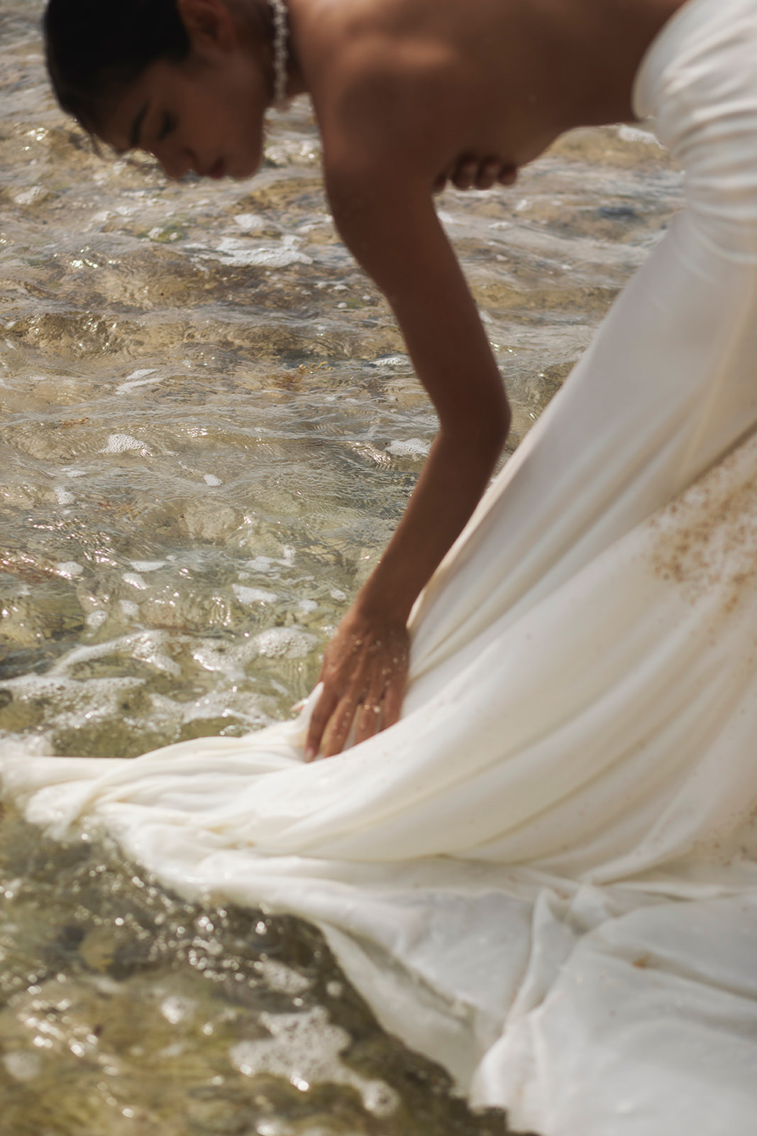 Blurry, in motion detail photo of bride in the ocean, featuring pearl-detailed bridal necklace. 