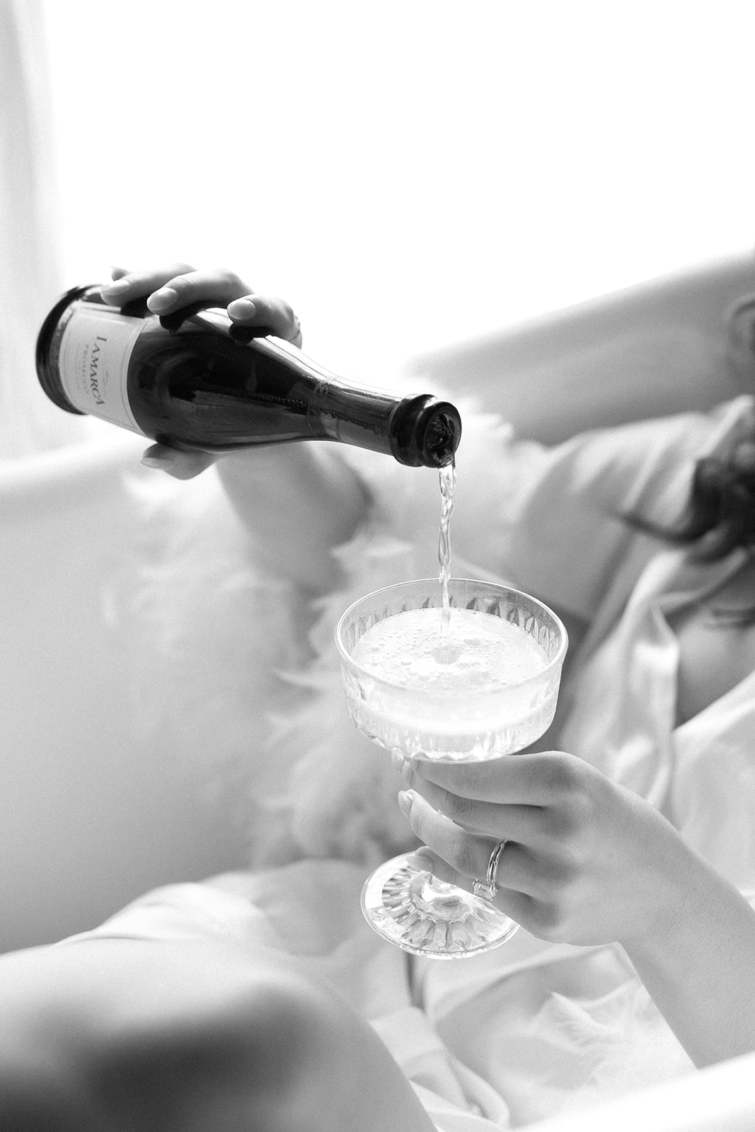 Bride relaxing in white clawfoot bathtub in the elegant vintage home, while pouring a glass of champagne. Morning-of Bridal Inspiration with Modern Style & Chic Getting Ready Photos.