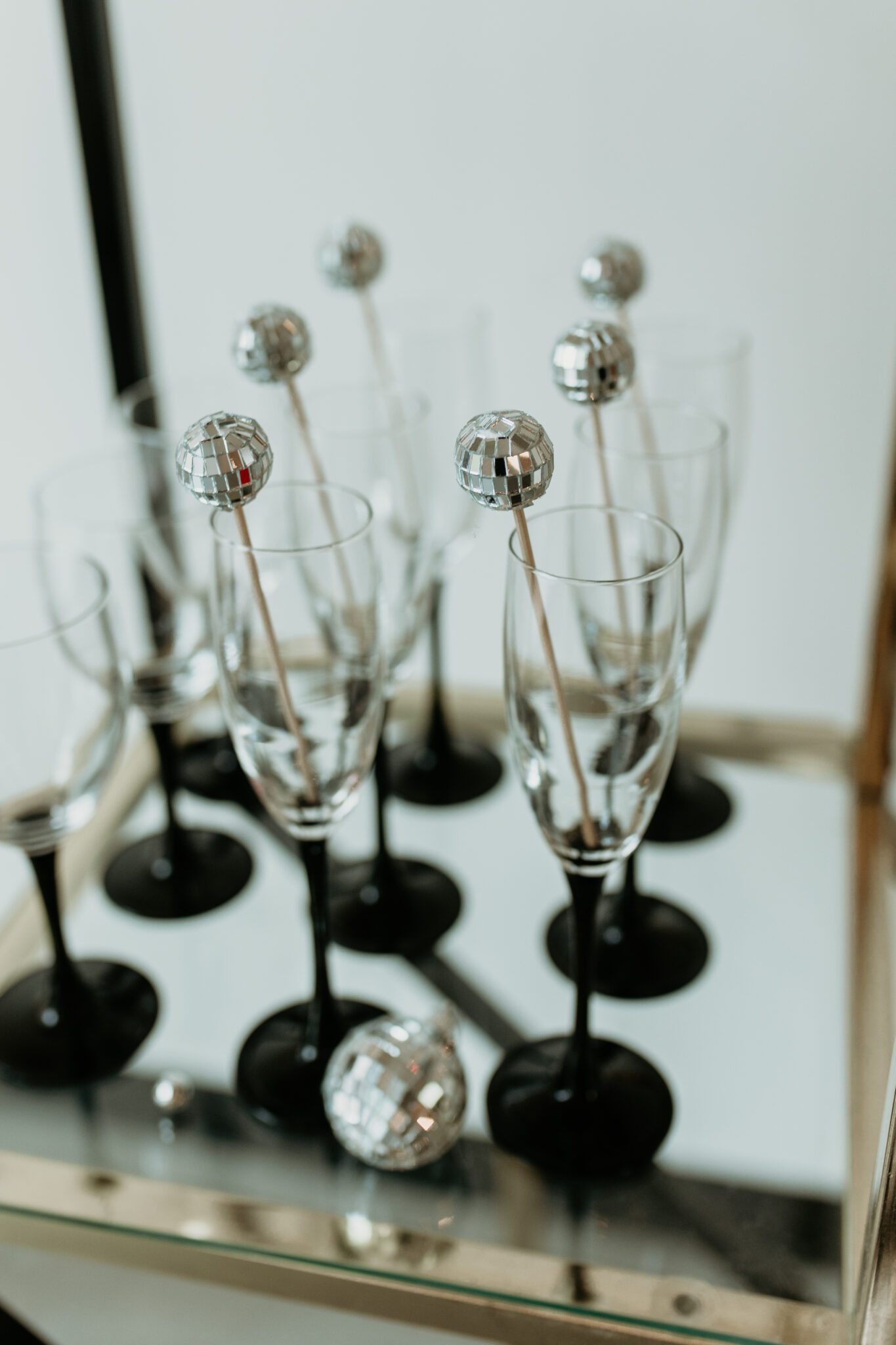 Chic wedding reception decor featuring a fusion of modern and retro aesthetics: modern decor elements alongside retro-inspired stationery and signage, black stemed champagne flutes styled with mini disco balls, creating a dynamic visual contrast.