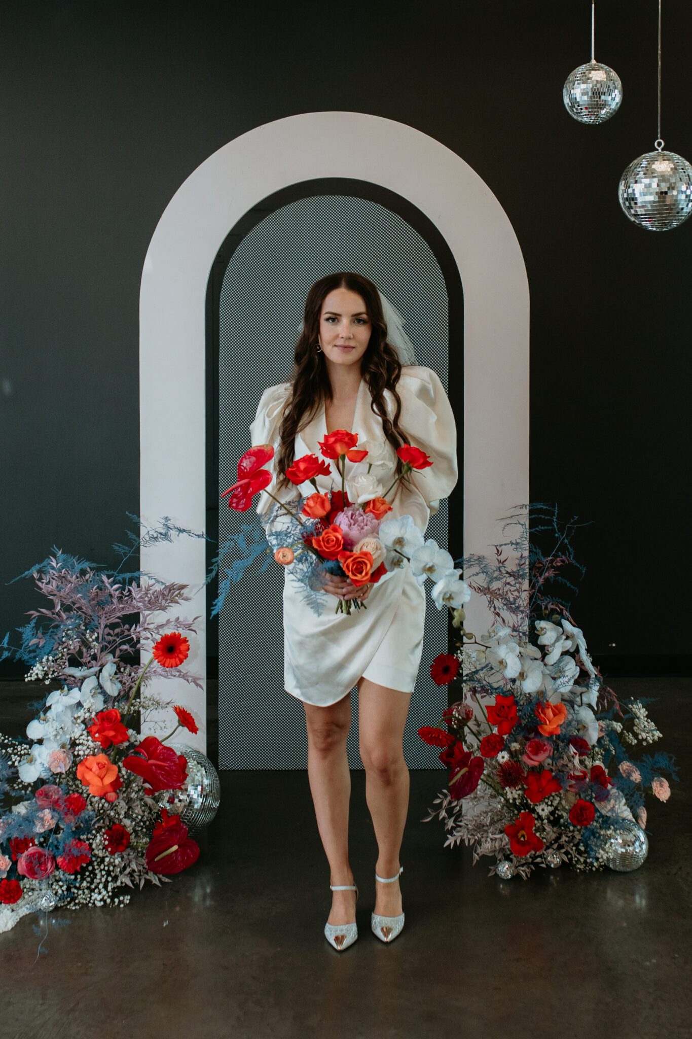 Chic bride standing in front of wedding decor seamlessly blending modern and retro styles, with eye-catching accents and retro-inspired stationery and signage contributing to the overall stylish atmosphere.