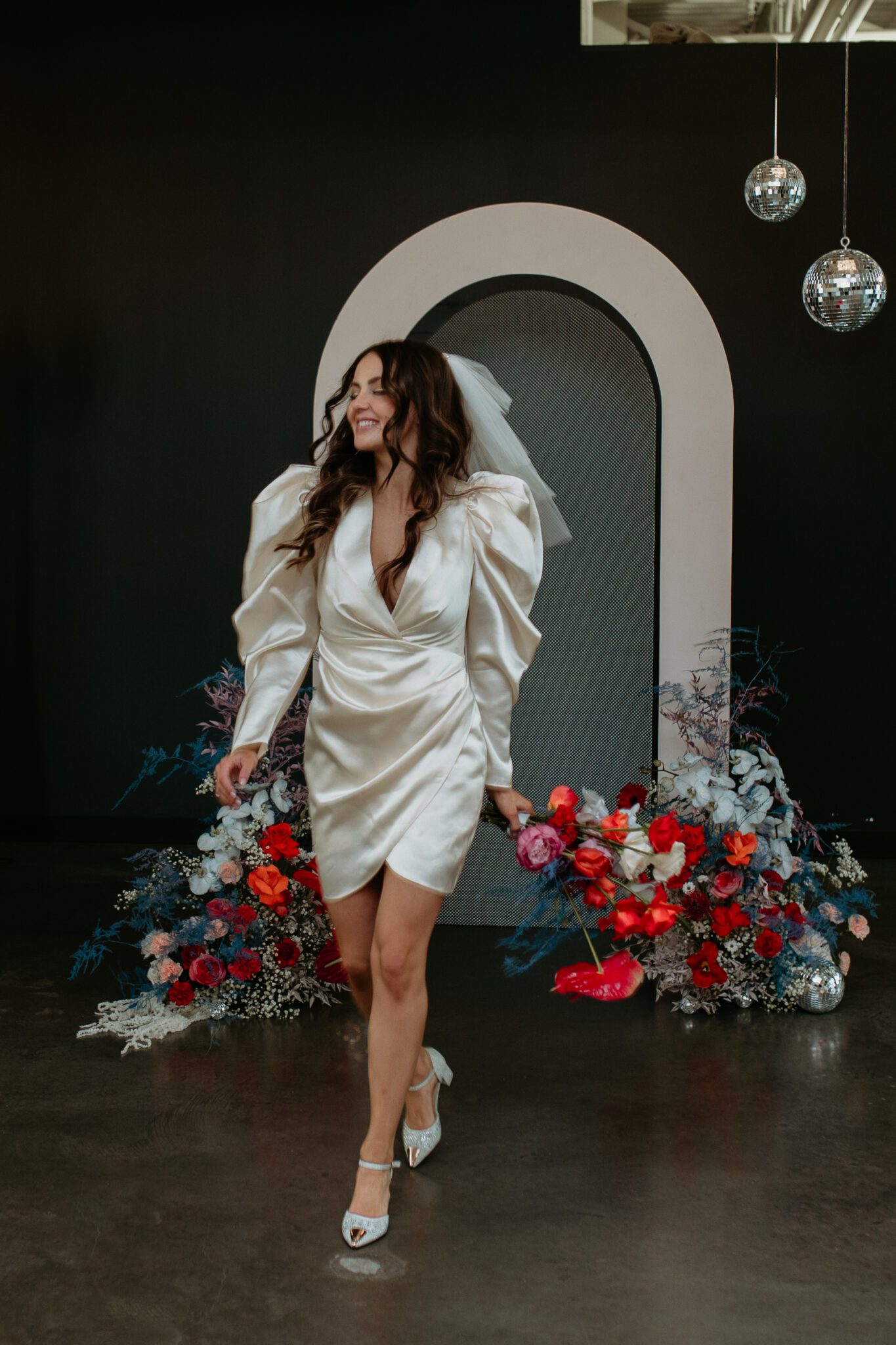 Chic bride standing in front of wedding decor seamlessly blending modern and retro styles, with eye-catching accents and retro-inspired stationery and signage contributing to the overall stylish atmosphere.