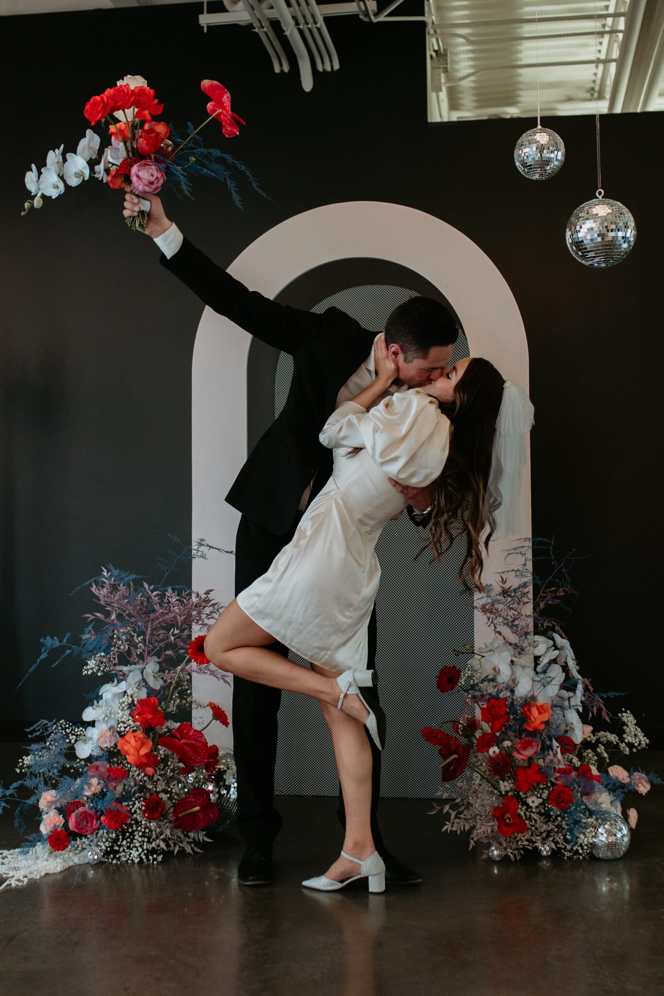 Couple kisses during bold retro-inspired wedding, combining vibrant colours, sleek lines, and nostalgic elements for a unique celebration.