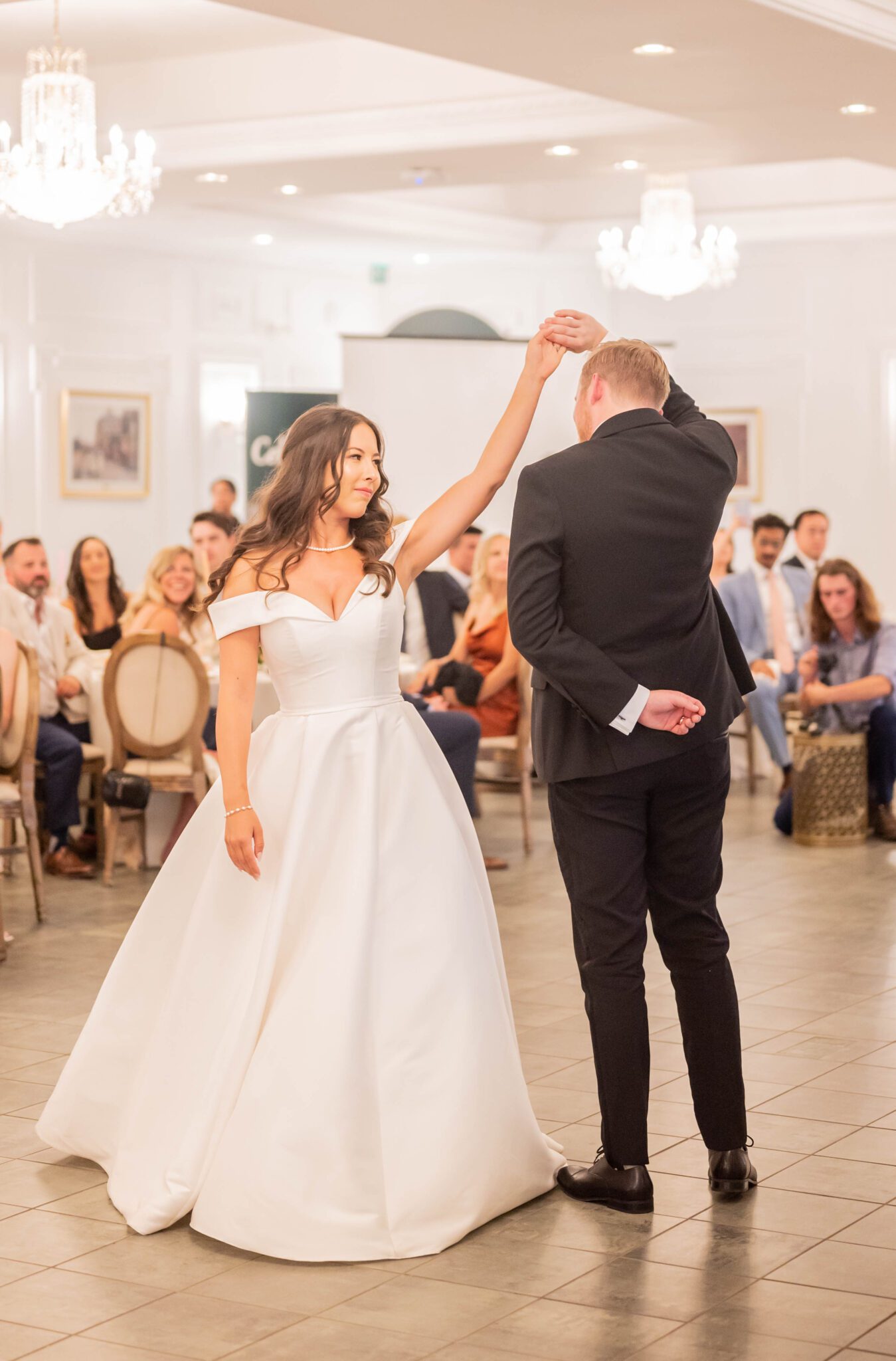 Couple shares their first dance as newlyweds at their garden party wedding reception at Spruce Meadows, bride wearing elegant gown with off the shoulder sleeves and sweetheart neckline.