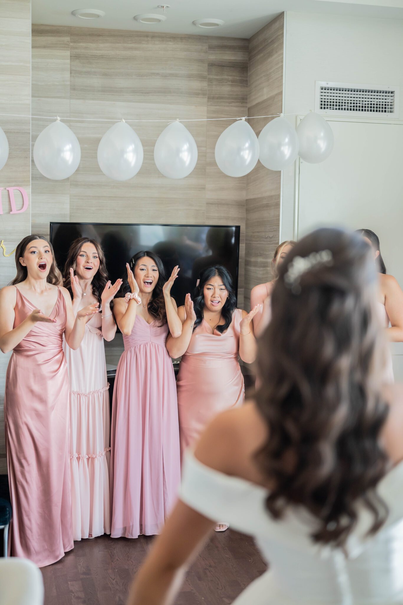 Bridesmaid first look reaction to bride in her elegant gown, bridesmaids in different shades of pink gowns, in getting ready suite.