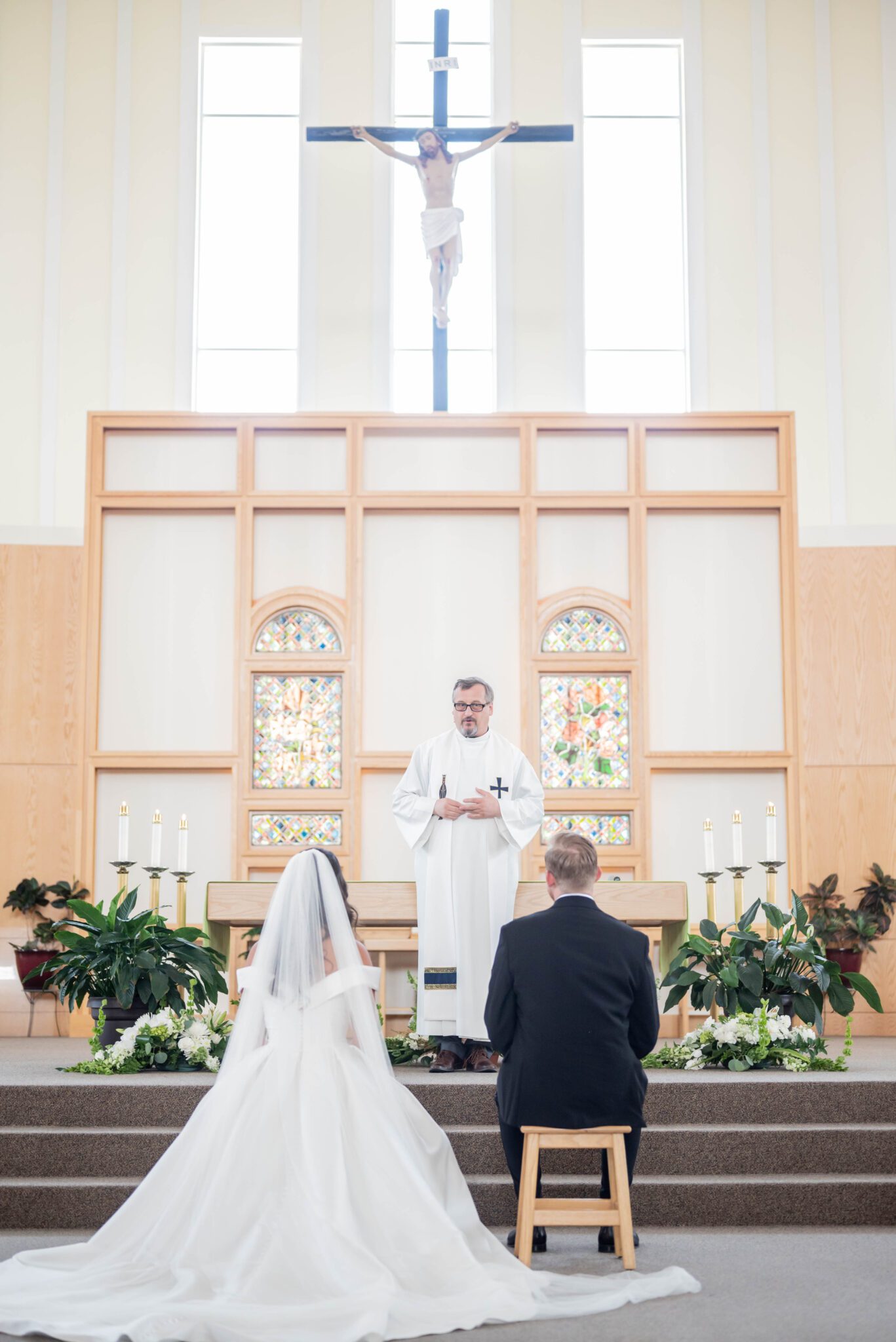 Couple sits in front of the ceremony altar at a Catholic church, bride in elegant long gown with cathedral veil.