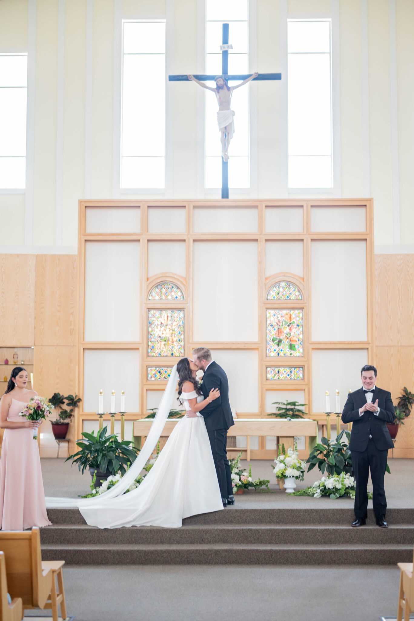 Bride and groom share their first kiss at the altar as husband and wife, in bright Catholic church. 