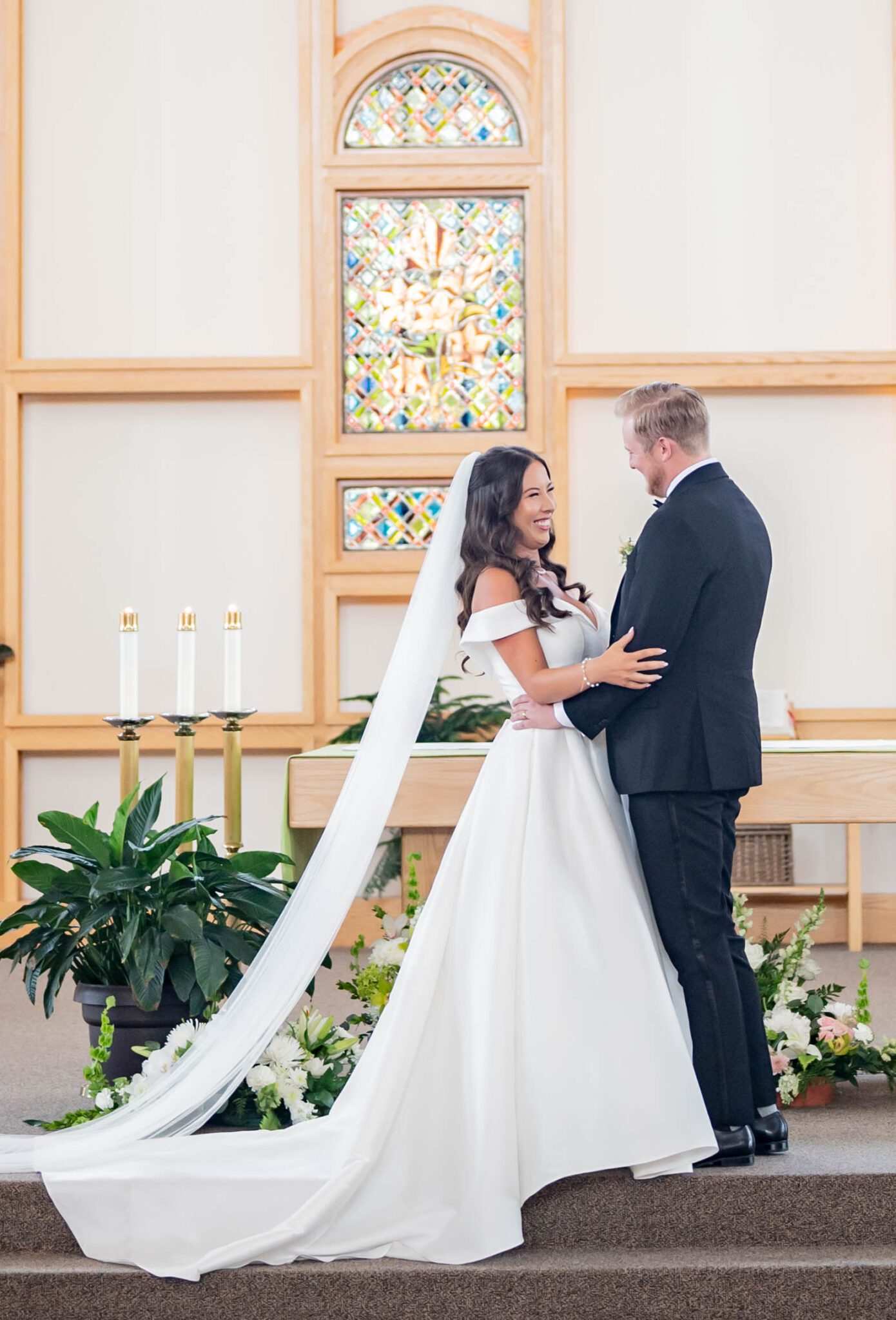 Bride and groom smiling after sharing their first kiss as husband and wife, featuring bride in elegant white gown with cathedral veil. 