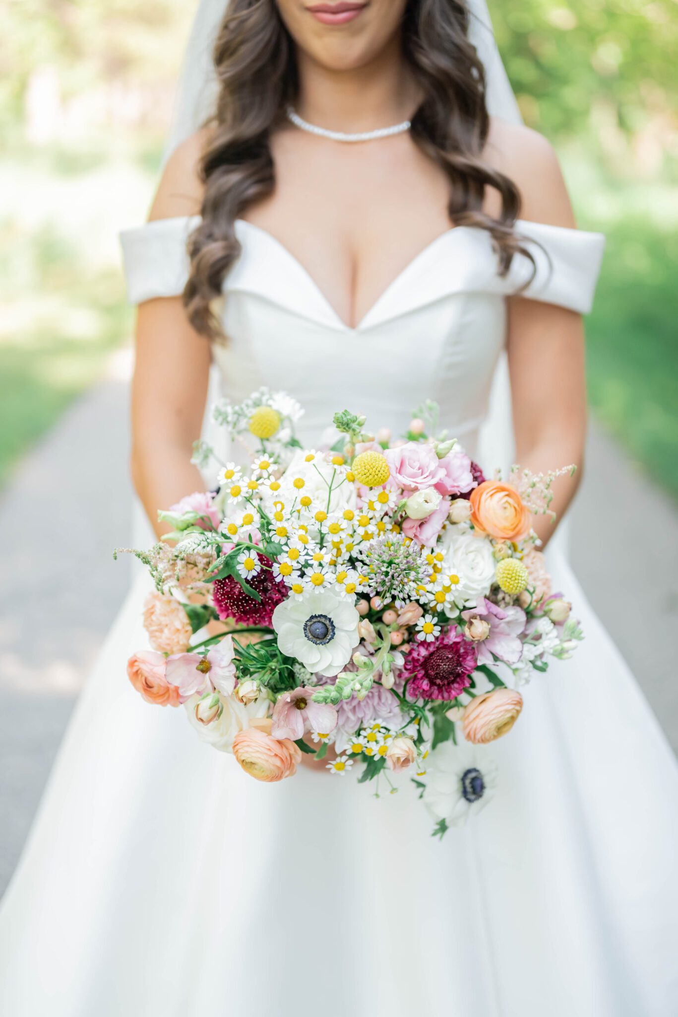 Close up portrait of bride's outfit details and wildflower bridal bouquet, featuring elegant bridal gown with off the shoulder sleeves and a sweetheart neckline. 
