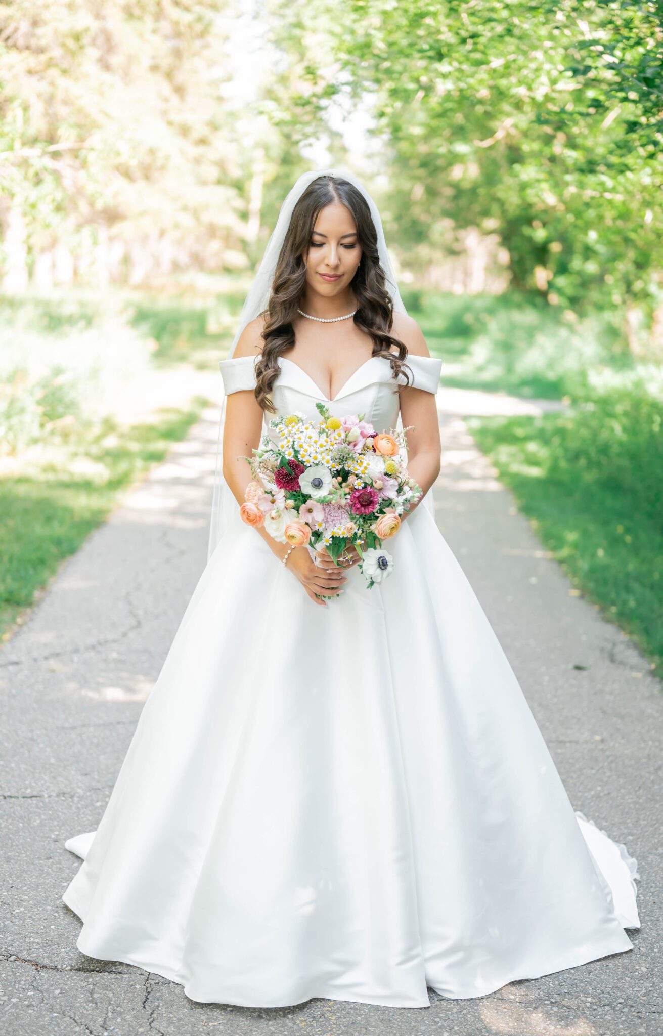 Portrait of bride's outfit details and wildflower bridal bouquet, featuring elegant bridal gown with off the shoulder sleeves and a sweetheart neckline, whimsical garden wedding in Spruce Meadows.