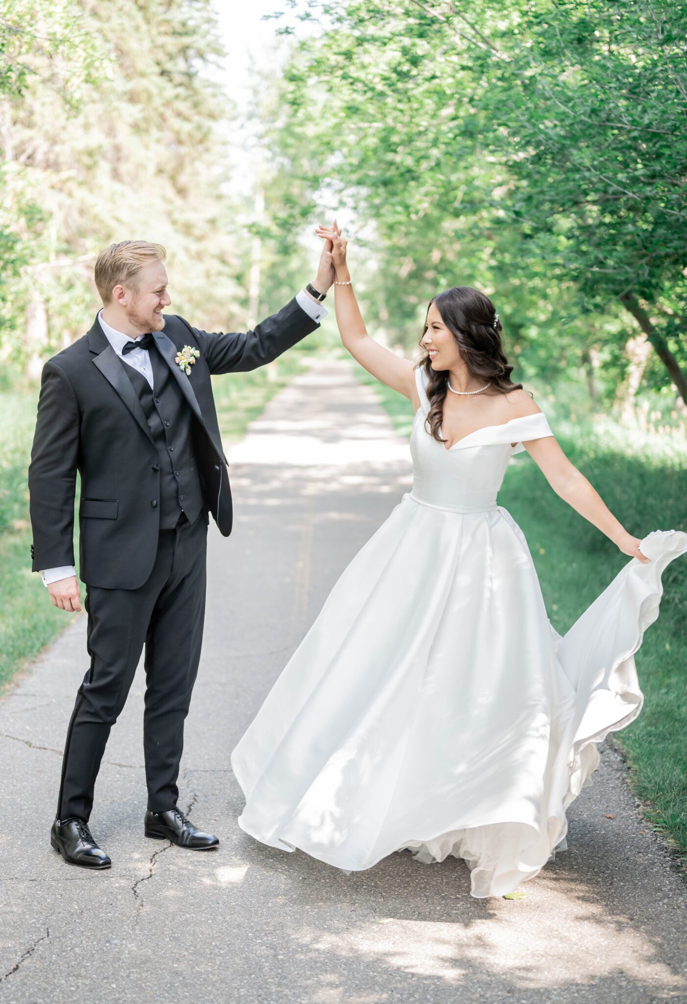 Groom twirls bride at their whimsical garden wedding in Spruce Meadows, bride wearing an elegant gown with off the shoulder sleeves and a sweetheart neckline. 