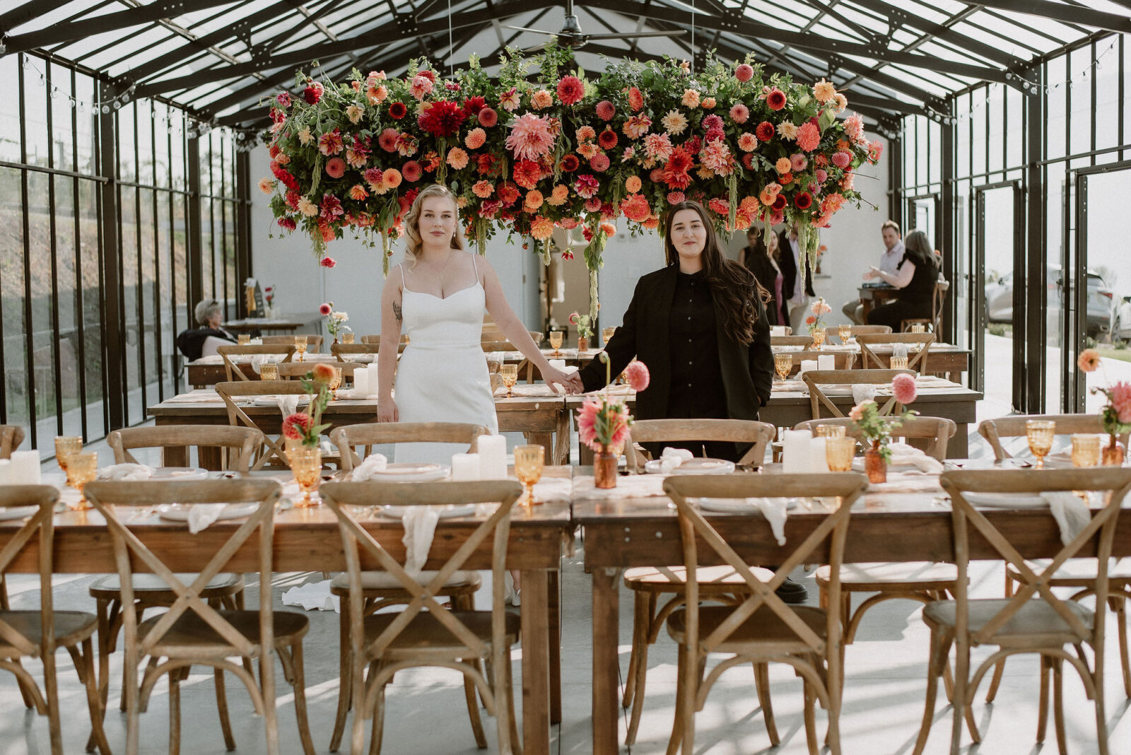 Portrait of brides standing in their wedding reception room at their vineyard wedding in the Okanagan, featuring colourful hanging floral installation.