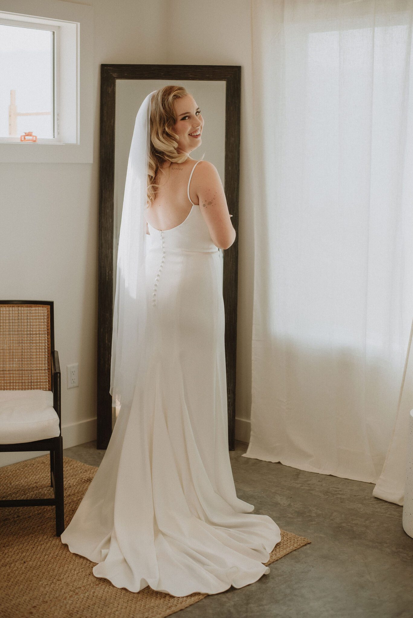 Bride getting ready for wedding in bridal suite, wearing an elegant gown with buttons down the backside of the dress with a long veil. 