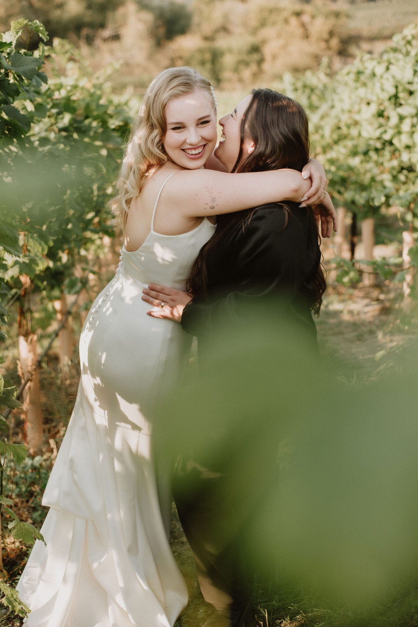 Couple embracing as they stand amongst the Okanagan vineyard at their intimate vineyard wedding with breathtaking views. 