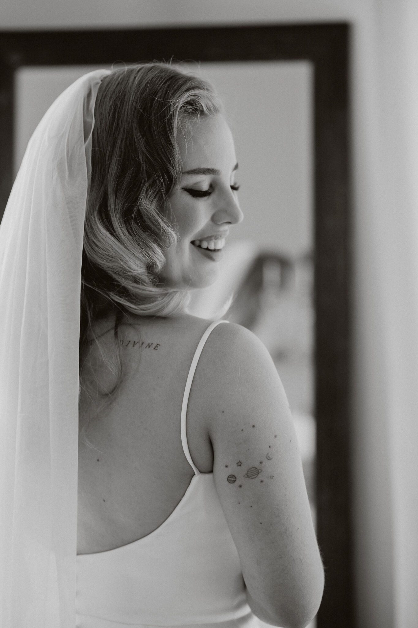 Bride smiling back towards the camera, wearing an elegant gown with buttons in the back and a long veil, black and white portrait inspiration. 