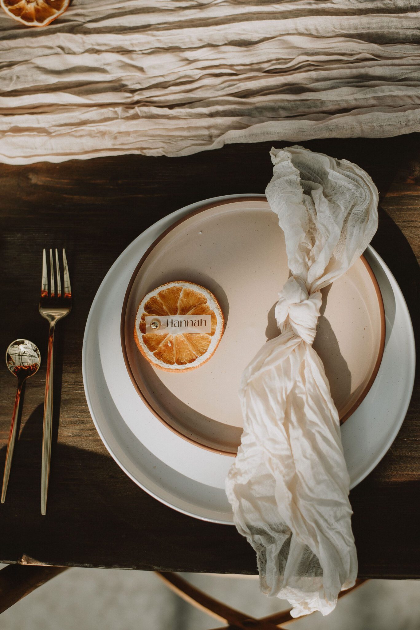 Close up portrait of wedding reception table setting details, with custom place cards set on top of a dried orange, featuring neutral colours for the plates and napkins. 