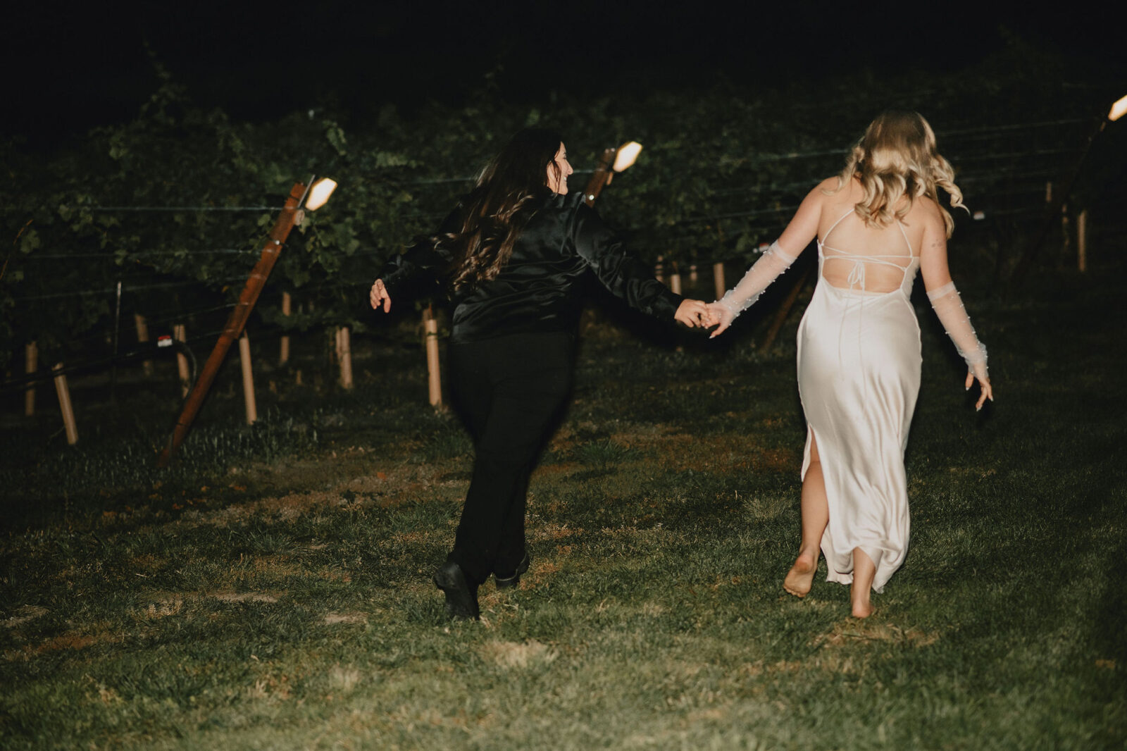 Flash portraits of brides embracing at their intimate vineyard wedding reception, featuring bride in silk mini dress with sheer gloves.