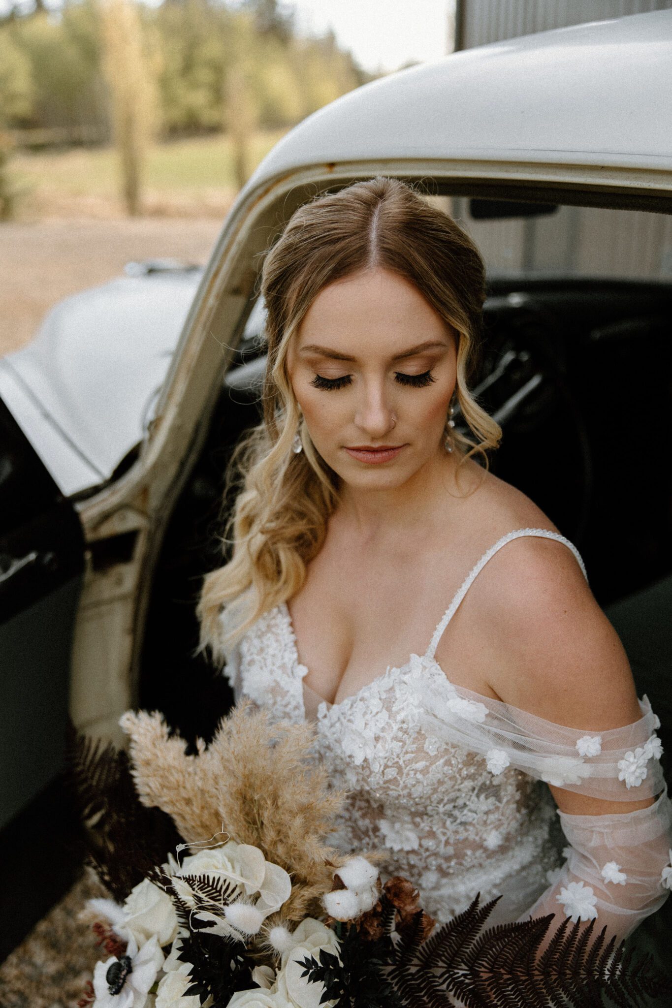 Portrait of bride sitting in the vintage getaway car at 52 North Venue, holding the bridal bouquet with rich textures and tones, wearing a floral detailed bridal gown with her hair in an elegant ponytail updo. 