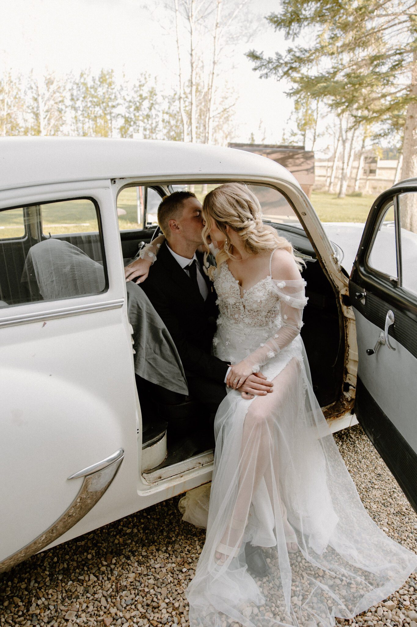Portrait of bride and groom sitting in their cream-coloured vintage getaway car, bride wearing a floral detailed tulle gown.