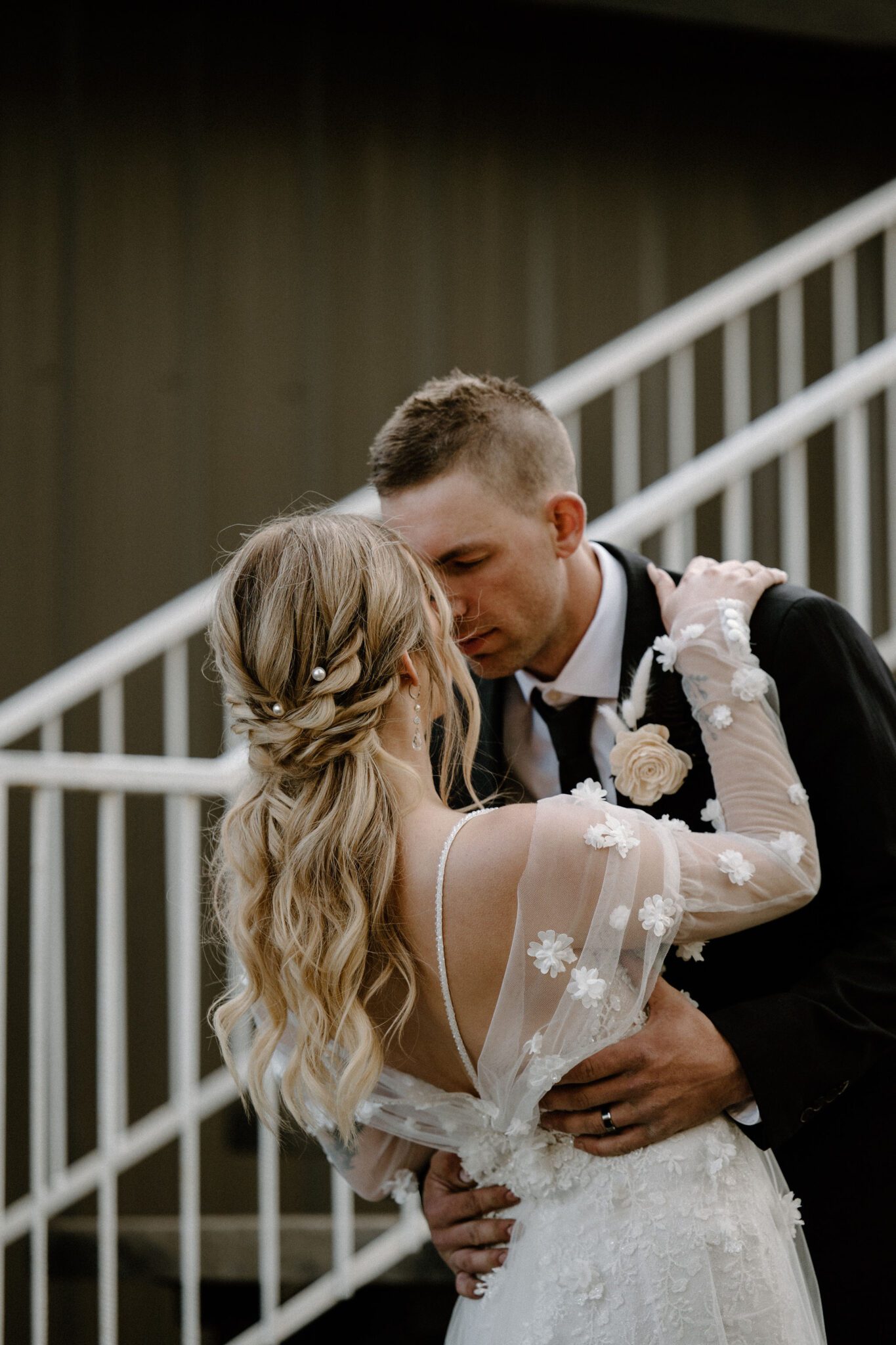 Portrait of bride and groom embracing at 52 North Venue, featuring bride's floral-detailed tule gown and elegant ponytail updo, warm and moody wedding inspiration. 