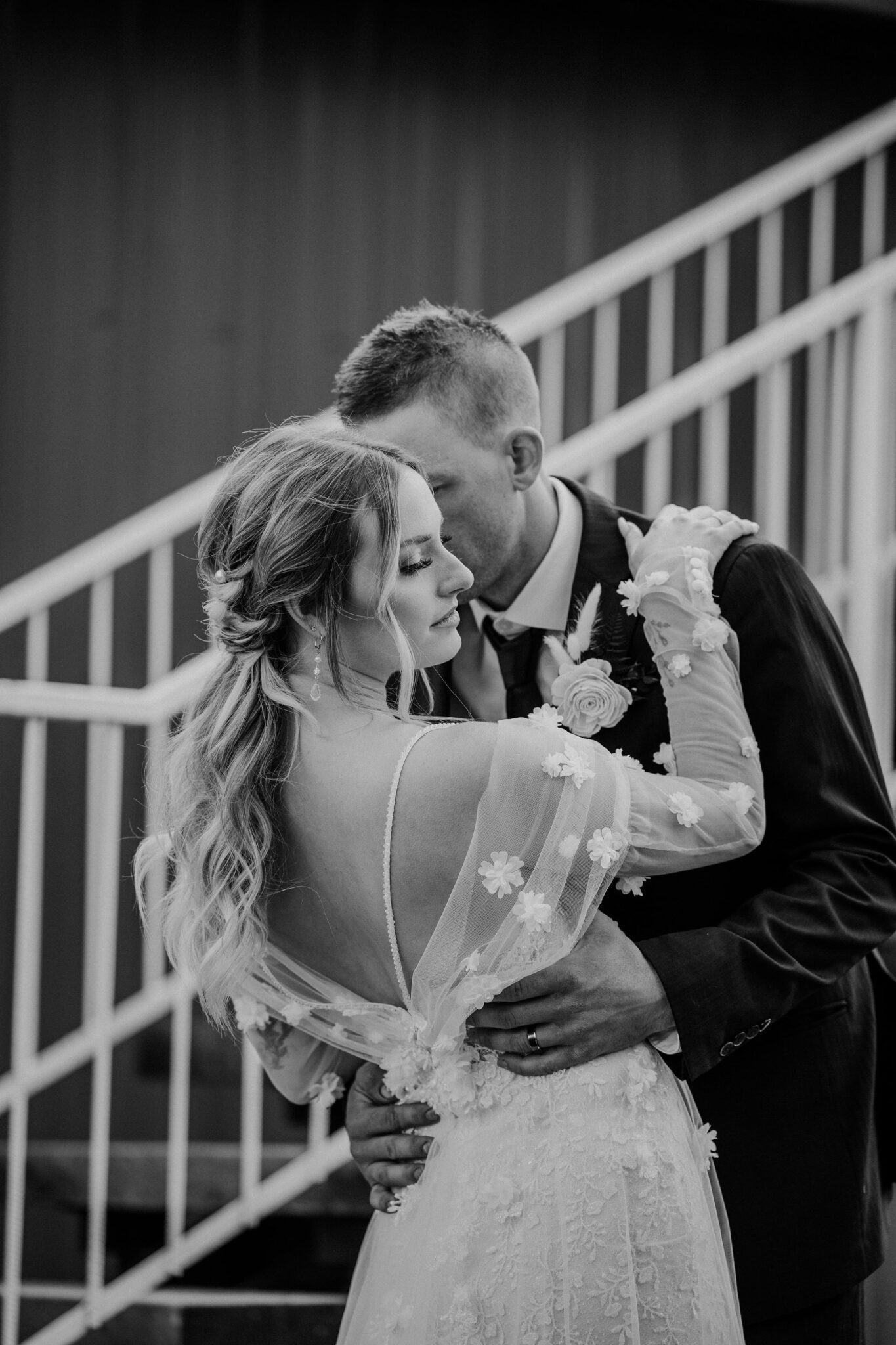 Black and white portrait of bride and groom embracing at 52 North Venue, featuring bride's floral-detailed tule gown and elegant ponytail updo, warm and moody wedding inspiration. 