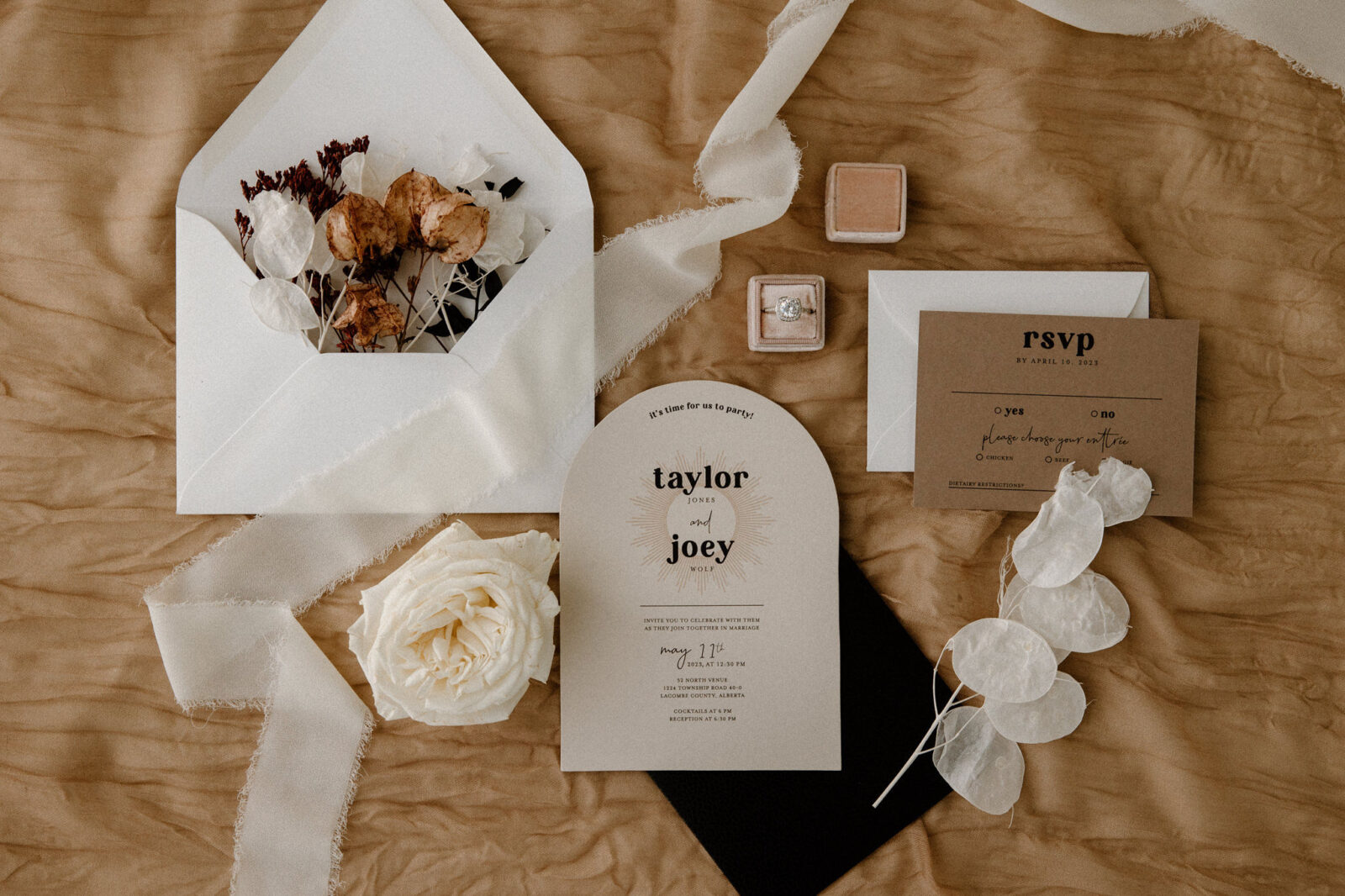 Flatlay details photo with brown-toned stationery, featuring a rose-coloured ring box with the bride's engagement ring.