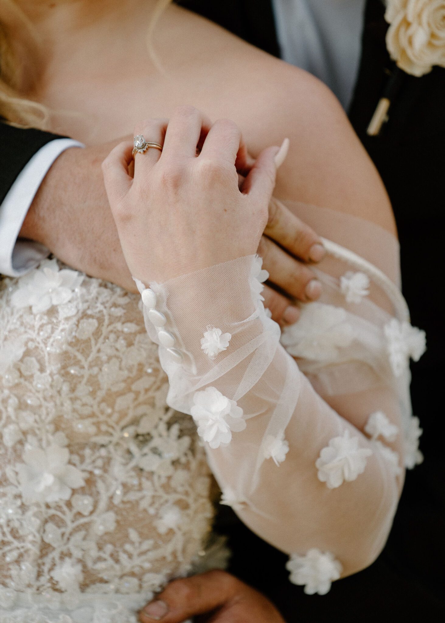 Close up, intimate portrait of groom embracing his bride, detailed photo of bride's ring and floral-detailed tulle gown, warm and moody wedding inspiration.