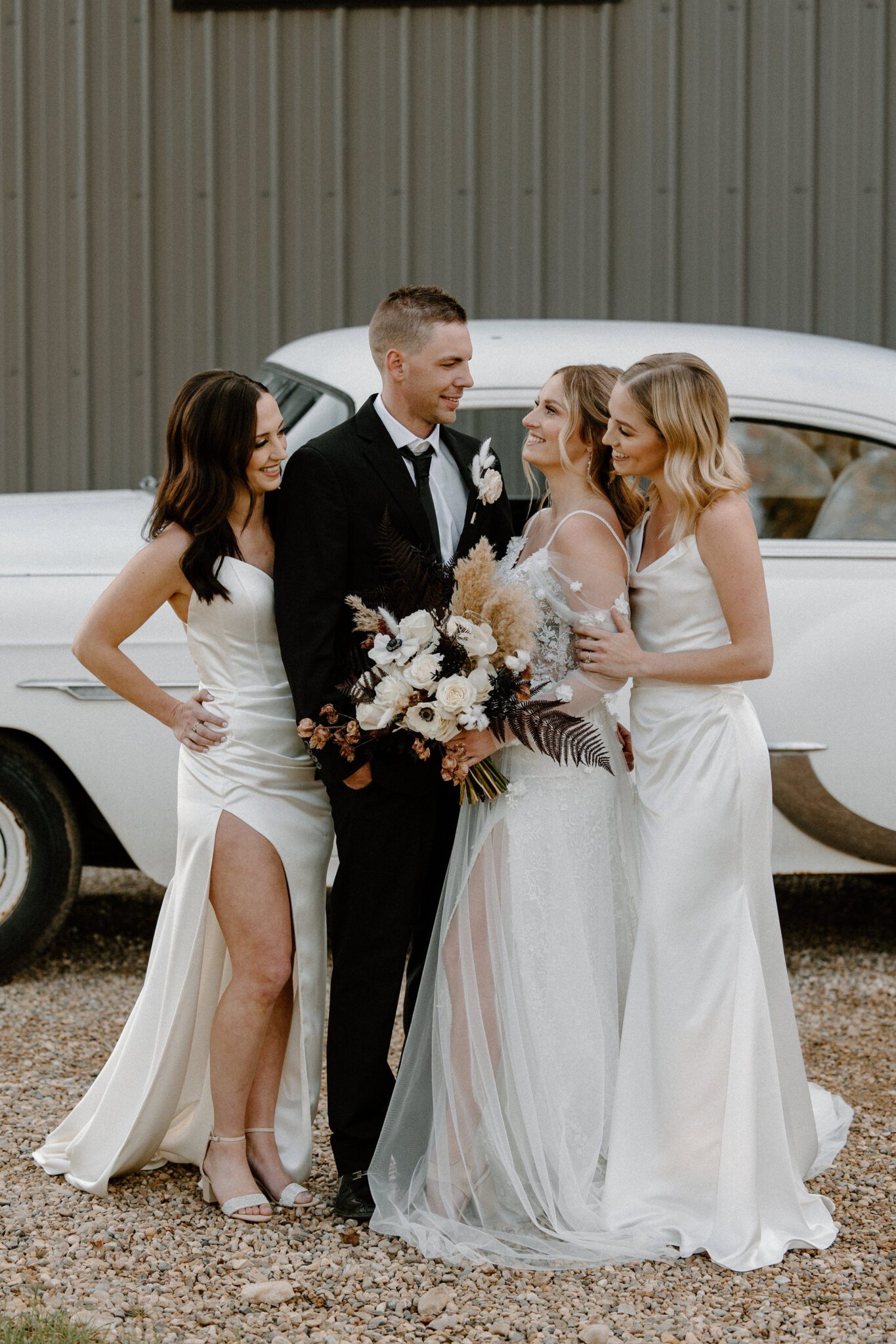 Portrait of bride and groom and bridesmaids, standing in front of cream-coloured vintage getaway car, warm and moody wedding inspiration at 52 North Venue. 