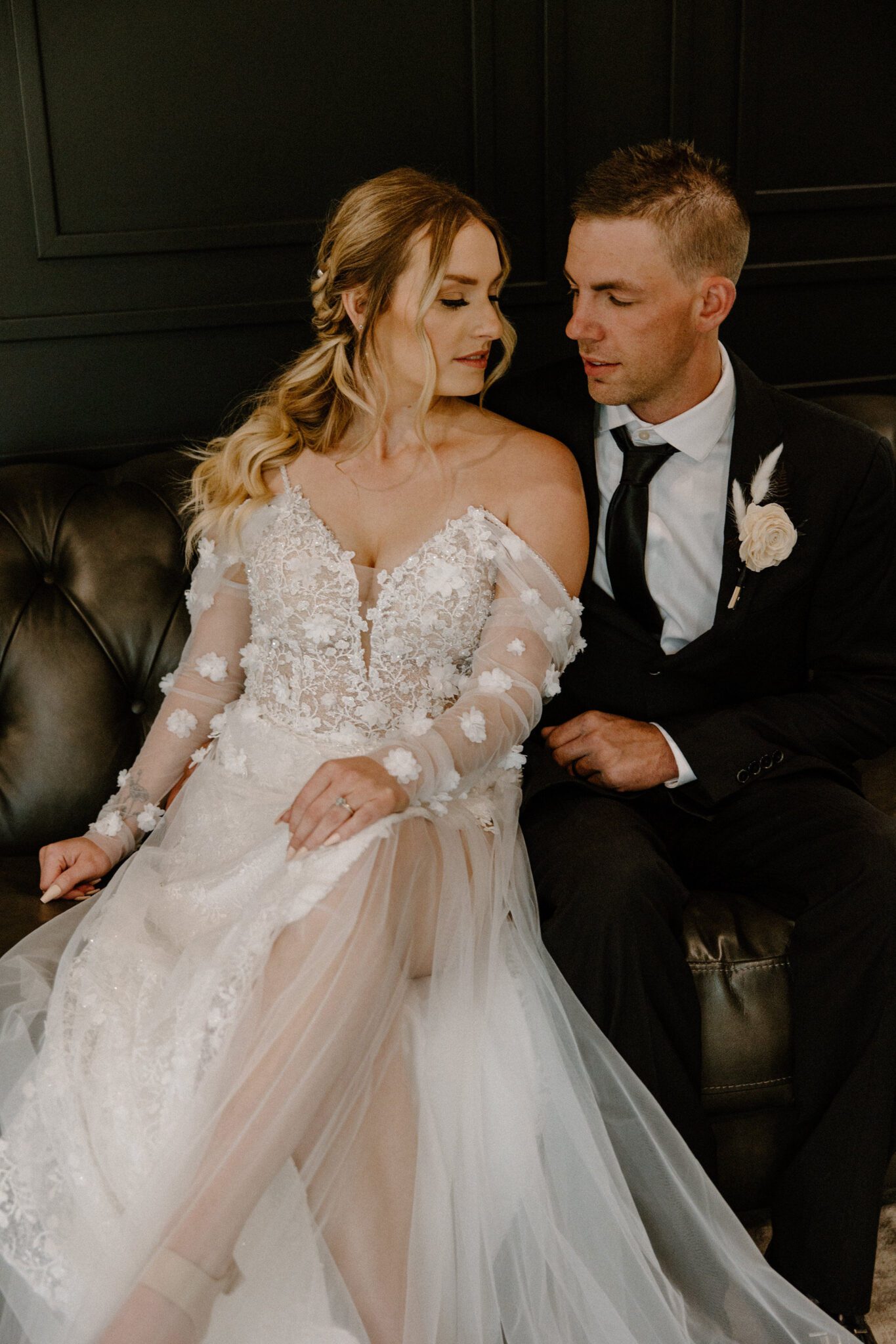 Indoor portrait of bride and groom sitting on vintage couch at 52 North Venue, bride in floral-detailed tulle gown, warm and moody wedding inspiration. 