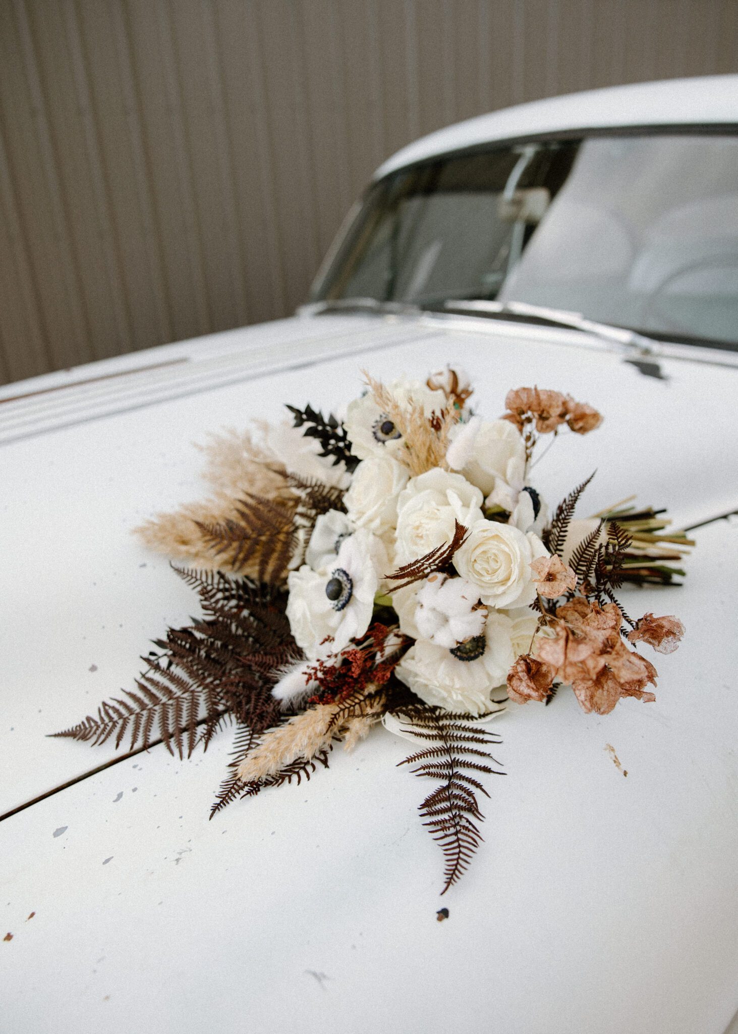 Detail photo of the bride's wedding bouquet with textured dried florals and rich tones, laying on top of the vintage getaway car.