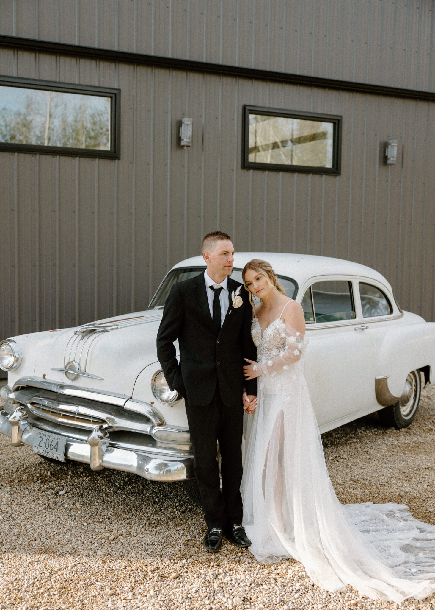 Bride and groom standing in front of vintage getaway car, bride in floral detailed tulle gown, warm and moody wedding inspiration at 52 North Venue. 