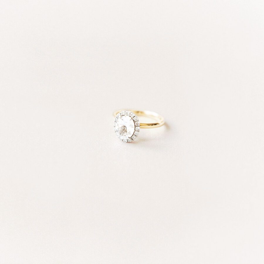 Close up portrait of an engagement ring with a halo diamond, and a simple gold band. 