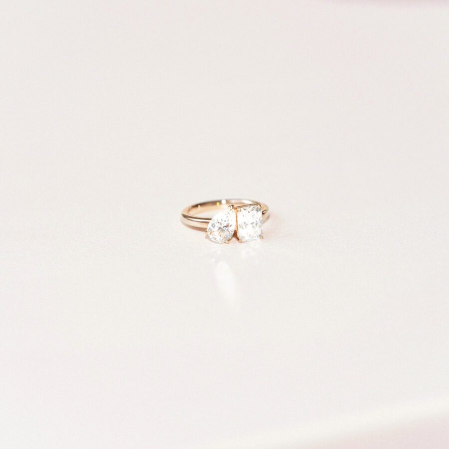 A close up portrait of a toi et moi engagement ring, with a simple gold band. 