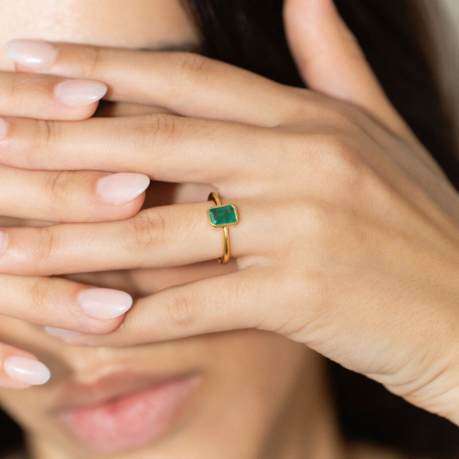 A bezel setting engagement ring with an emerald green gemstone, and a simple gold band. 