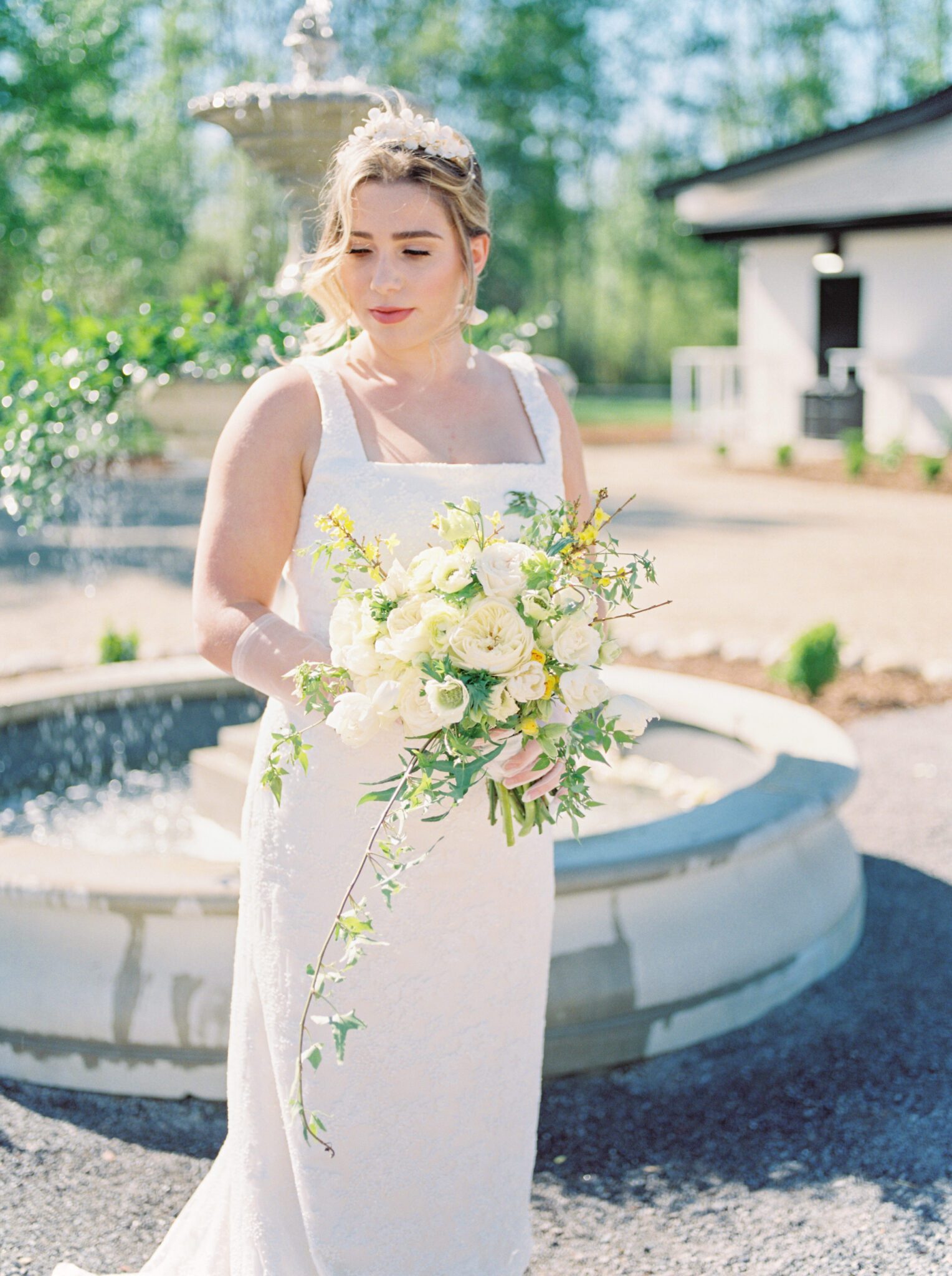 Bride standing in front of the water fountain at Sparrow Lane Events,  holding pale yellow and ivory bouquet for the perfect spring wedding inspiration. 