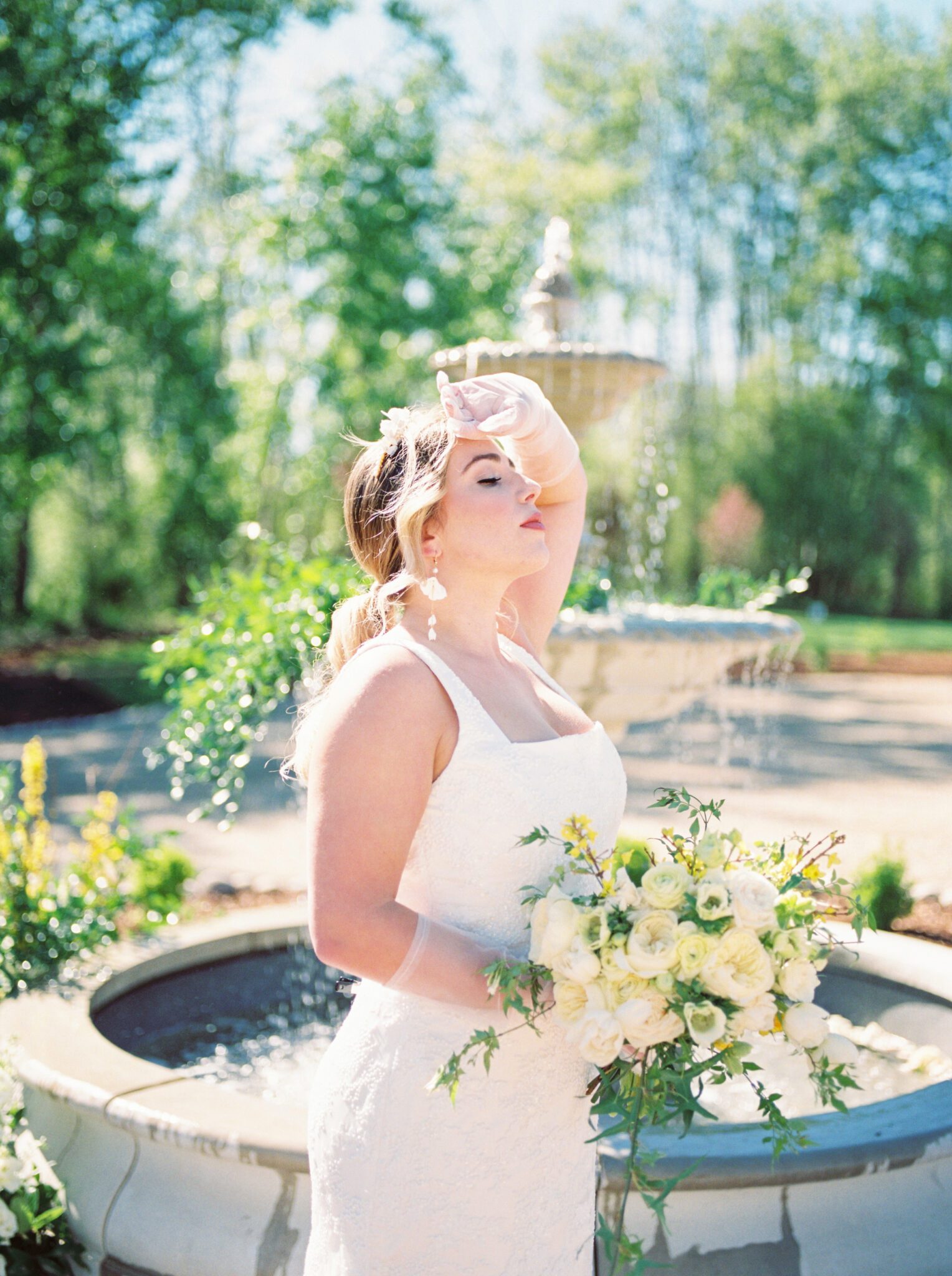 A beautiful bride wearing floral and pearl headpiece by Joanna Bisley Designs, and wearing sophisticated yet whimsical bridal gown. Outdoor spring wedding inspiration, bridal bouquet of pale yellow flowers, ivory roses and peonies with greenery. 