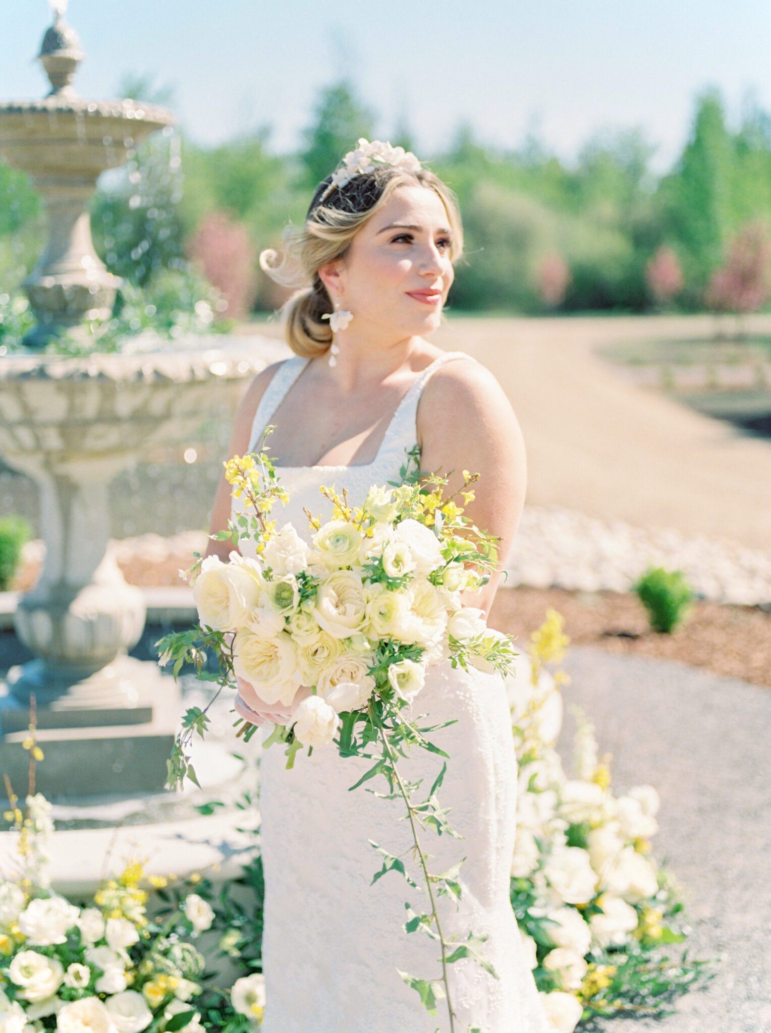 Elegant bride wearing a sophisticated yet whimsical bridal gown from Delica Bridal and floral jewellery by Joanna Bisley Designs, holding pale yellow and ivory floral bouquet for the perfect spring wedding inspiration. 