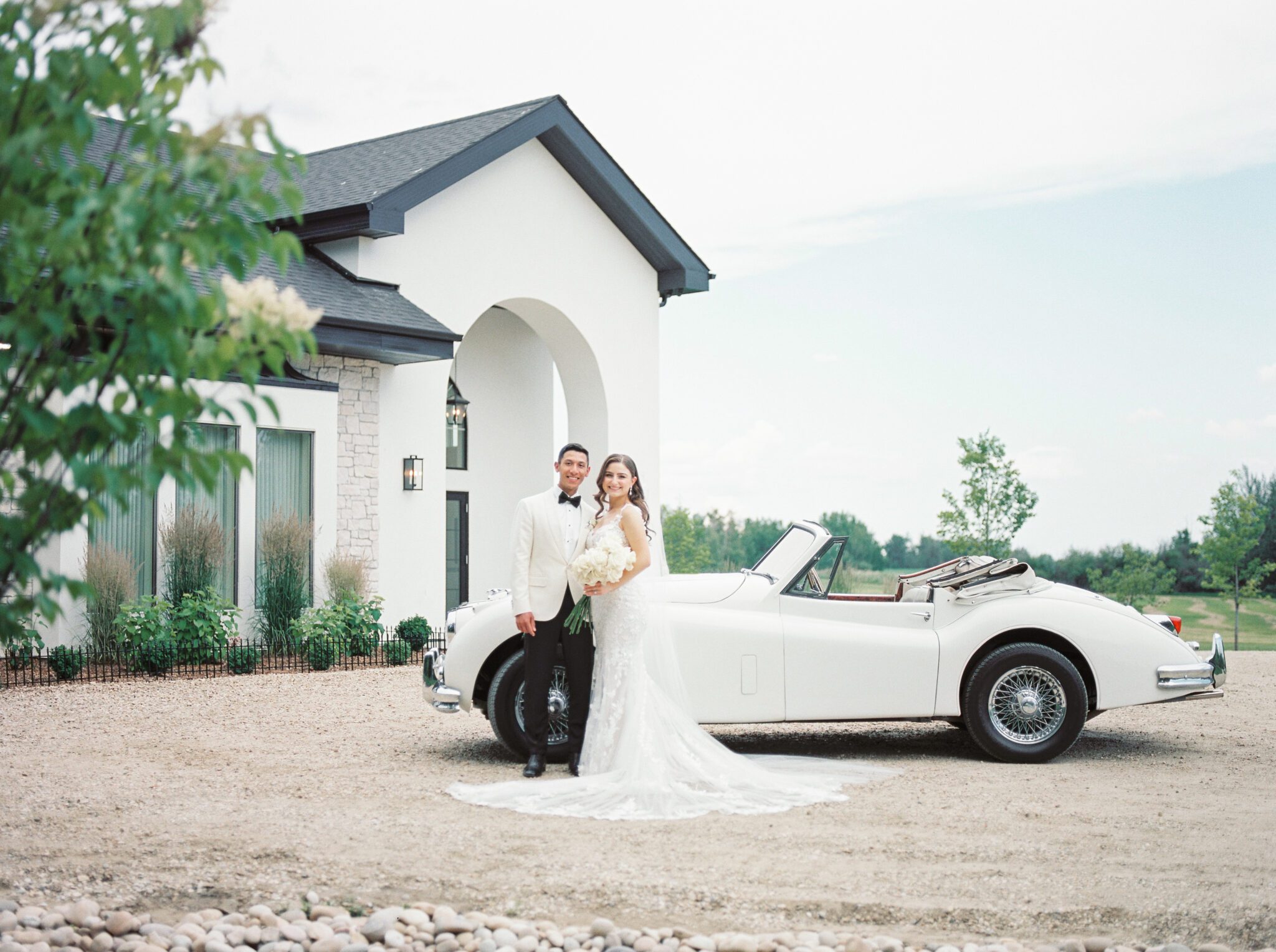Elegant bride and groom with a vintage car outside of Sparrow Lane Events in Alberta. Classic colour palette of white, blush, and green wedding inspiration. Timeless Summer Wedding.