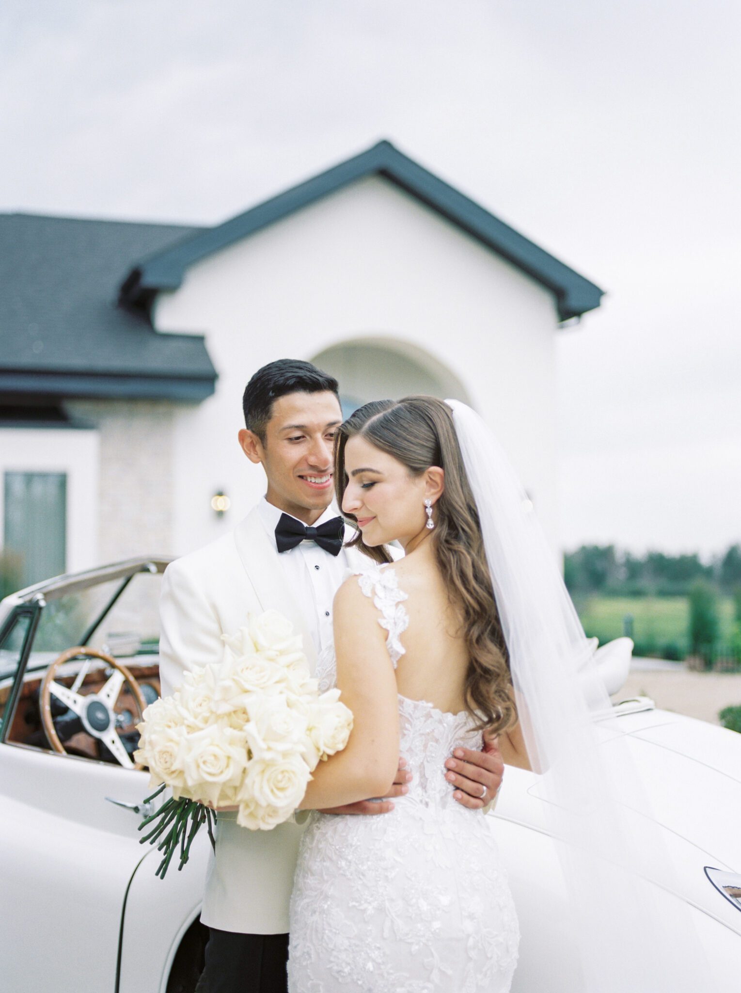 Elegant bride and groom with a vintage car outside of Sparrow Lane Events in Alberta. Classic colour palette of white, blush, and green wedding inspiration.
