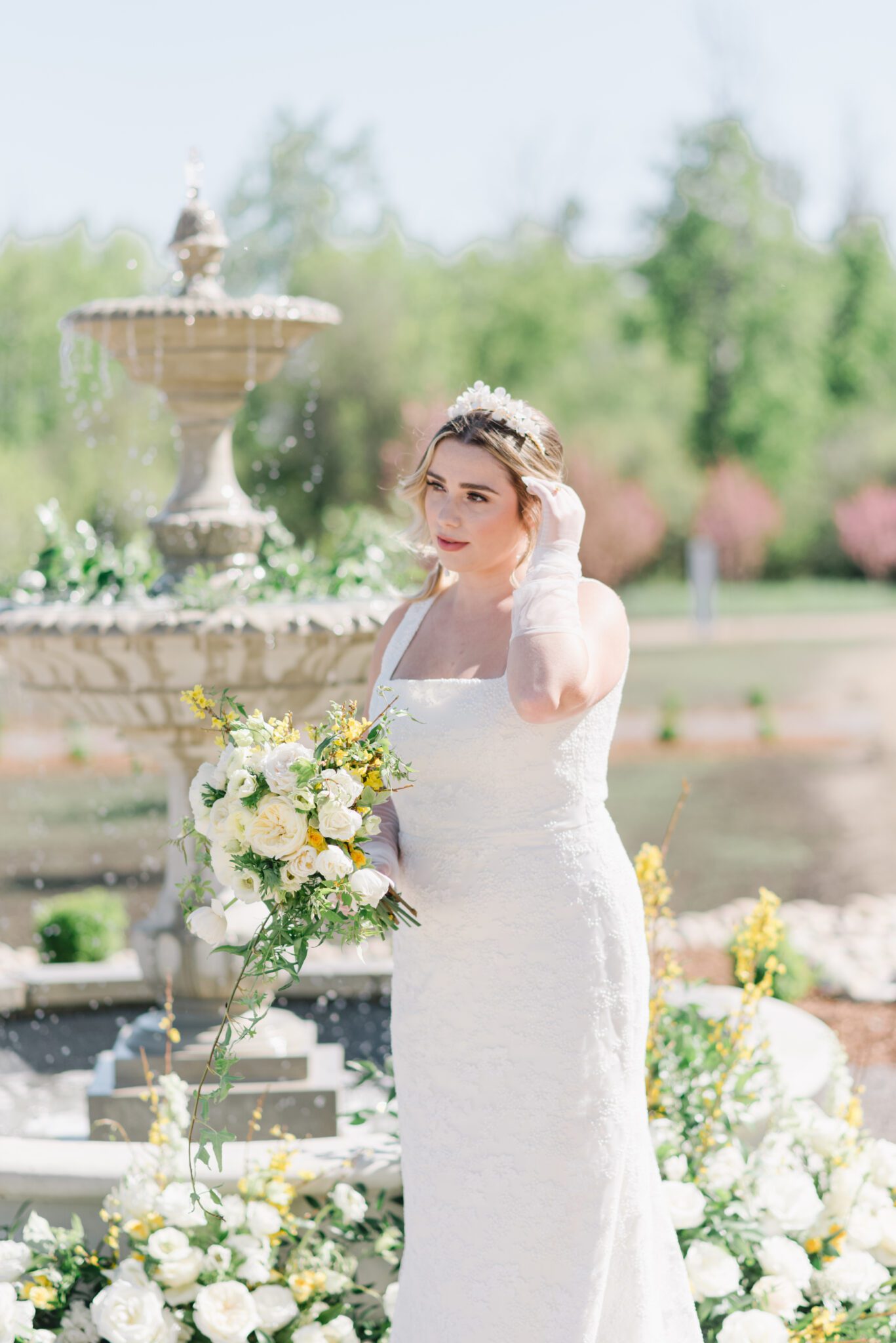 Gorgeous bride standing in front of the water fountain at Sparrow Lane Events,  holding pale yellow and ivory bouquet for the perfect spring wedding inspiration. 