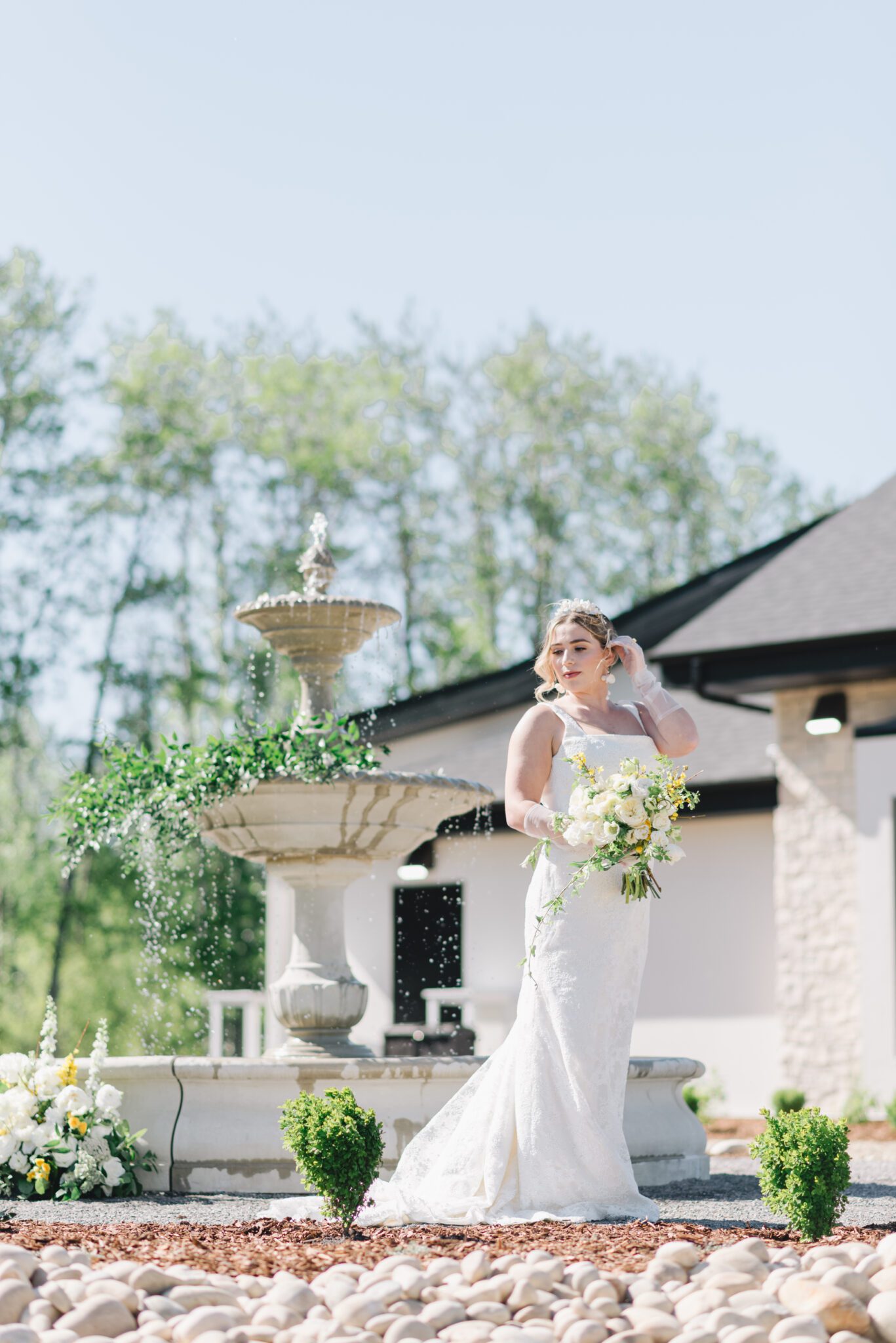 Bride standing in front of the water fountain at Sparrow Lane Events,  holding pale yellow and ivory bouquet for the perfect spring wedding inspiration. 
