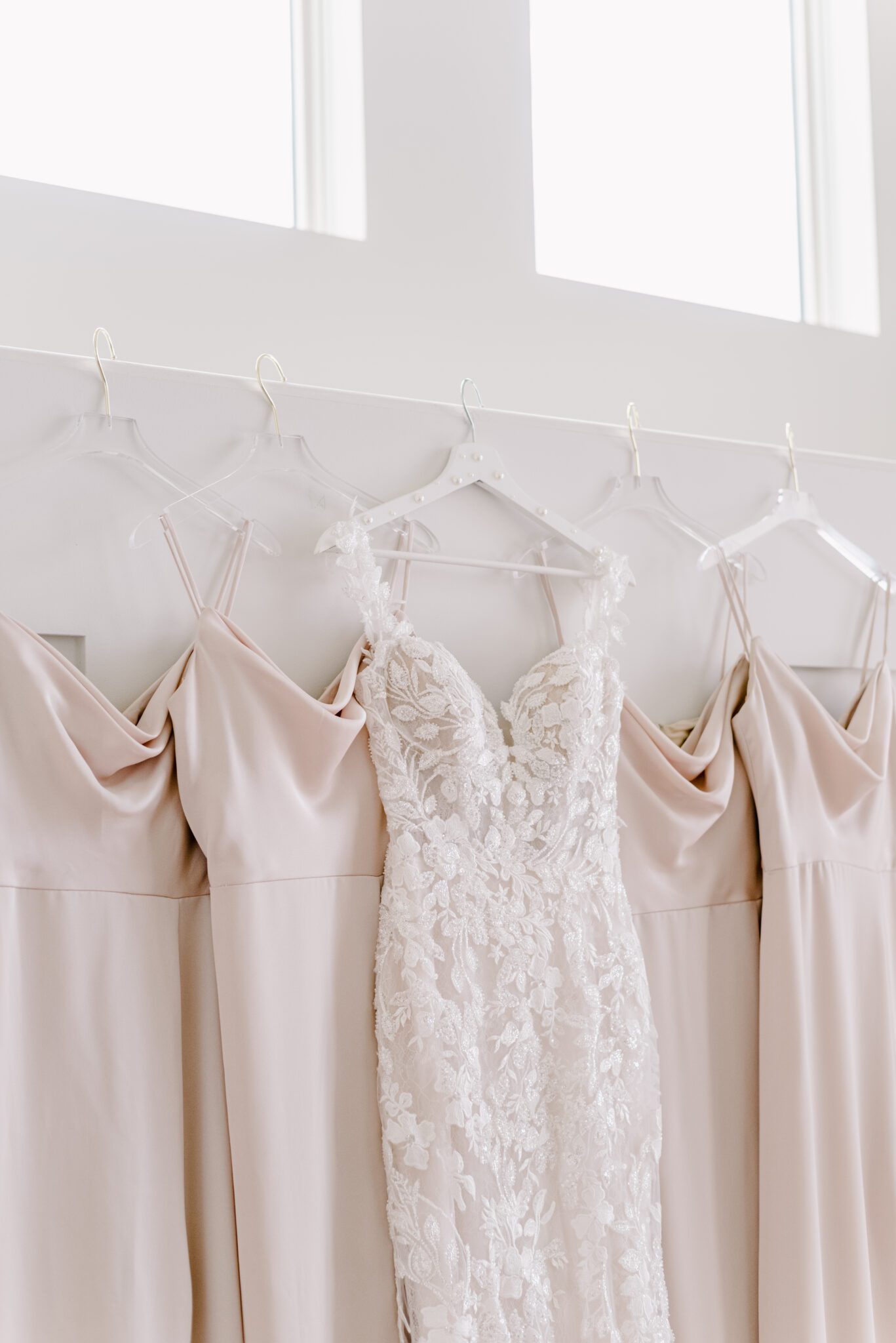 Lace bridal gown from Cameo & Cufflinks, hanging with blush Hayley Paige bridesmaids dresses.