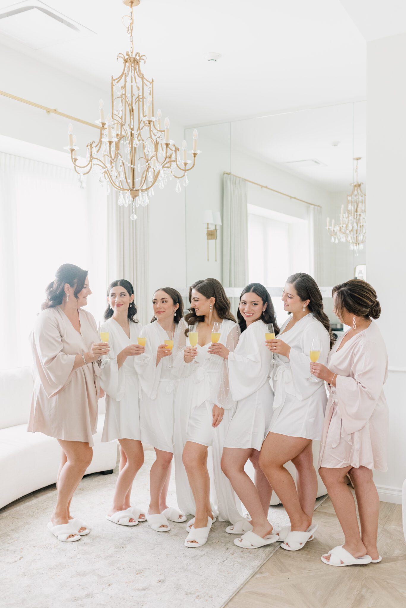 Stunning bride getting ready for her wedding day, drinking mimosas with bridesmaids, wearing elegant bridal robes.