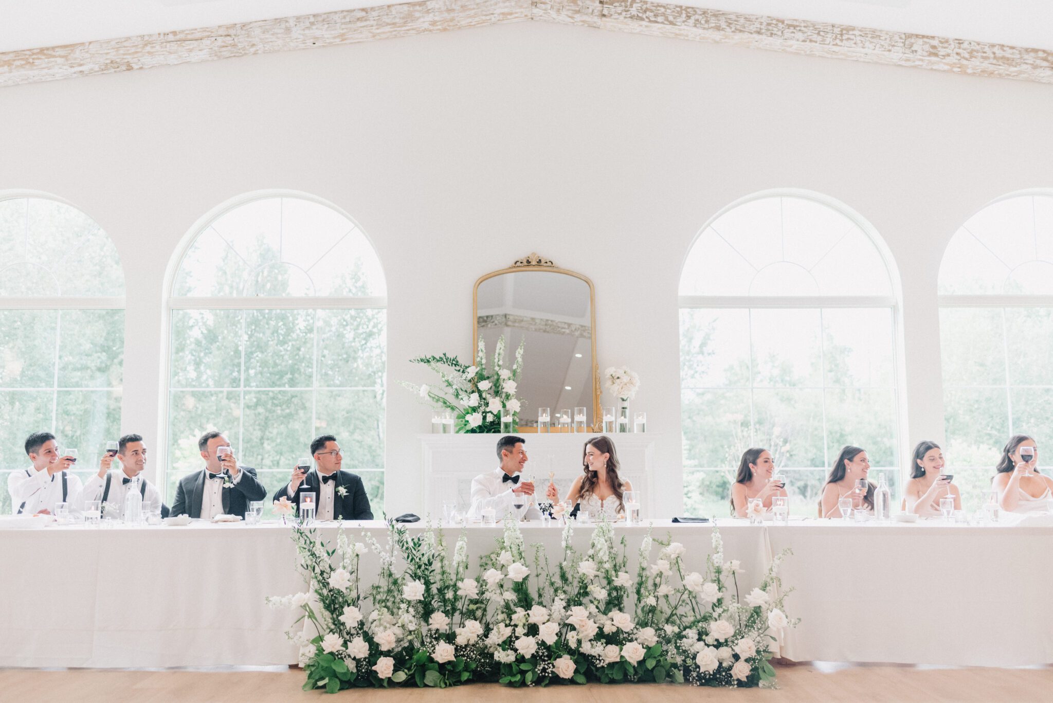 Elegant summer wedding reception at Sparrow Lane Events in Alberta. Summer wedding features white roses, greenery blush decor accents and warm wood tones.