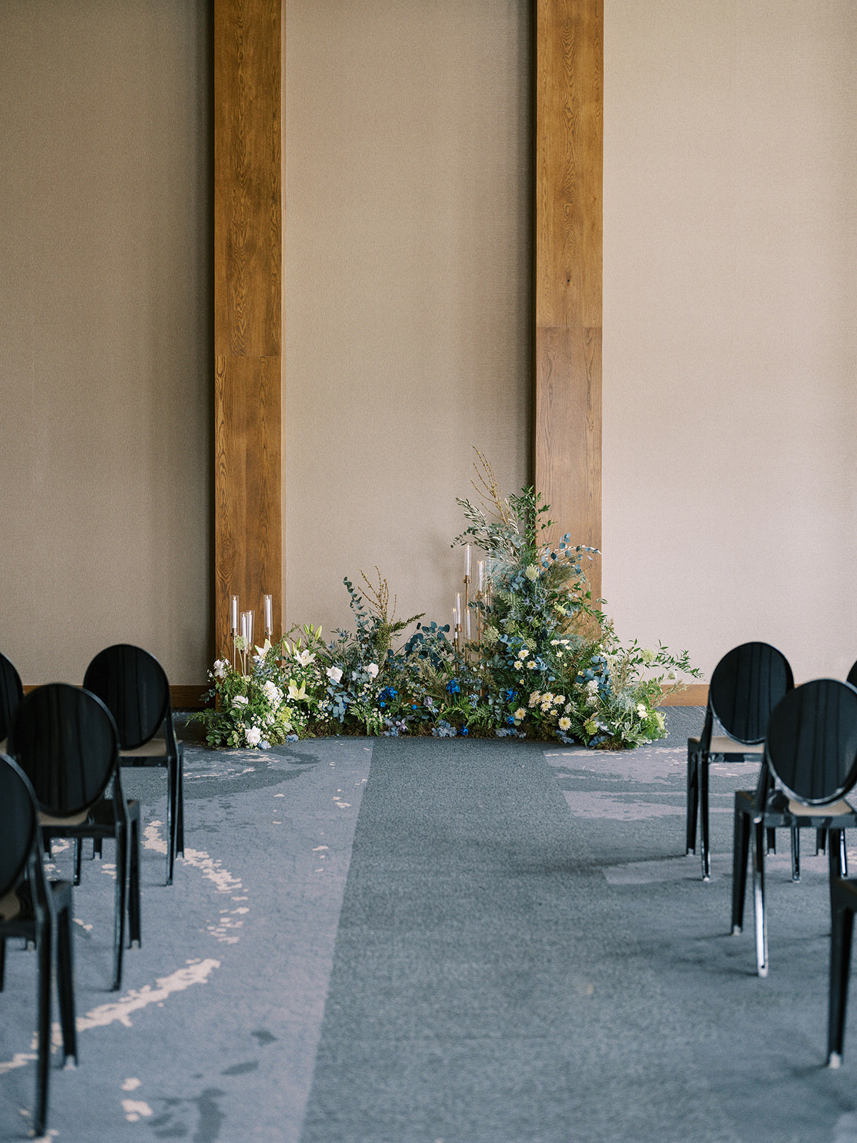 Contemporary and romantic wedding ceremony at The Malcolm Hotel in Canmore, Alberta; grounded floral arch for an indoor wedding ceremony with black ghost chairs