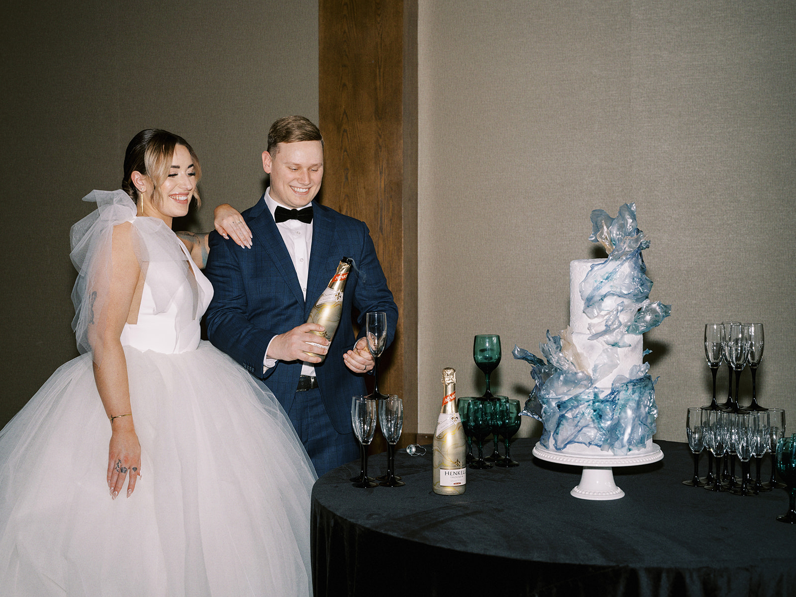 Bride and Groom popping champagne, contemporary and elegant cool-toned wedding cake by Bake My Day at The Malcolm Hotel featuring Mediterranean-inspired decor in oceanic colour palette. 